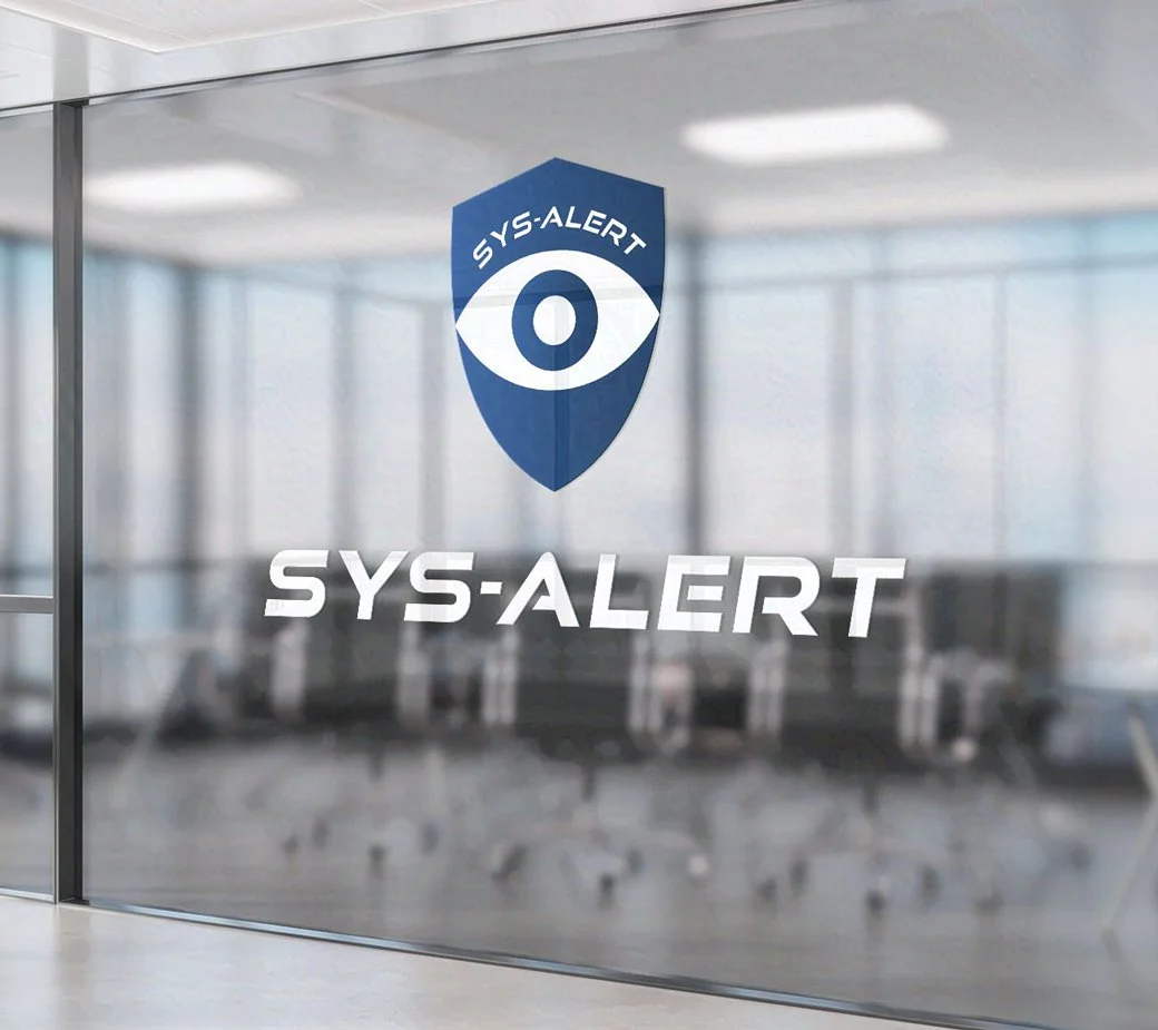 A glass office wall displays a blue shield logo with an eye and the text SYS-ALERT below it, overlooking a modern, empty conference room.