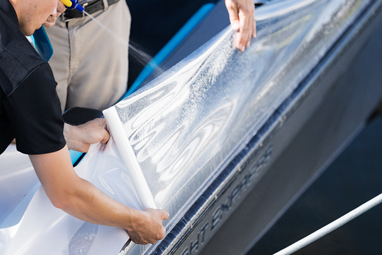People applying a protective vinyl wrap to the side of a black car.