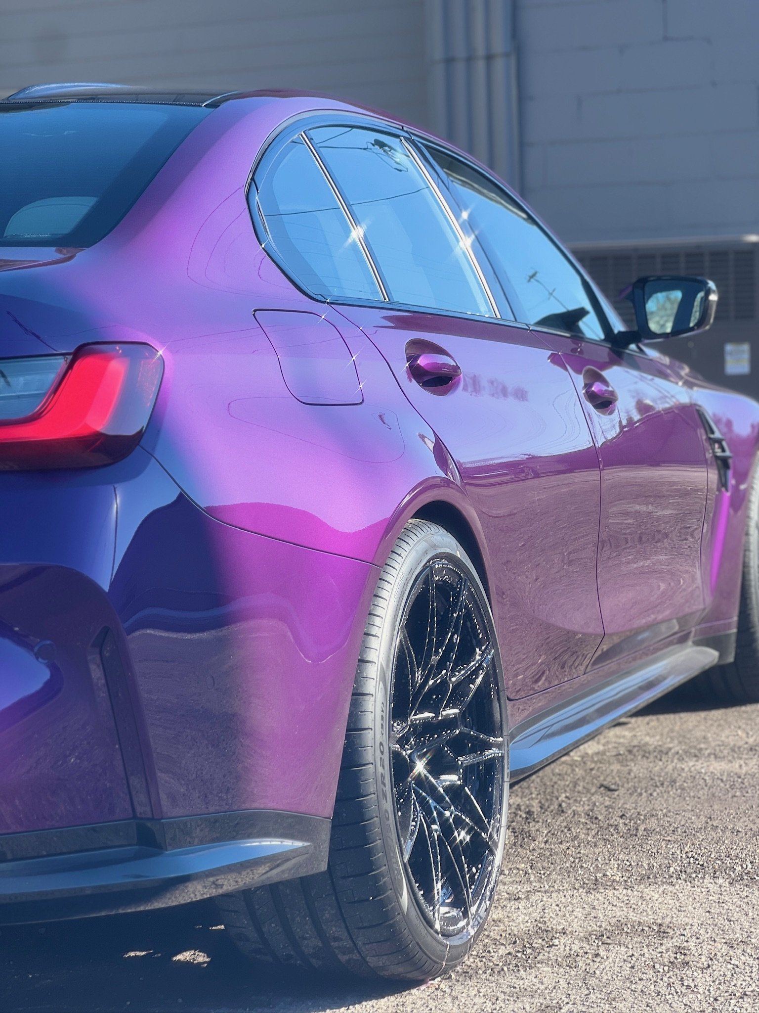 A purple futuristic sports sedan with black wheels parked on a gravel lot.