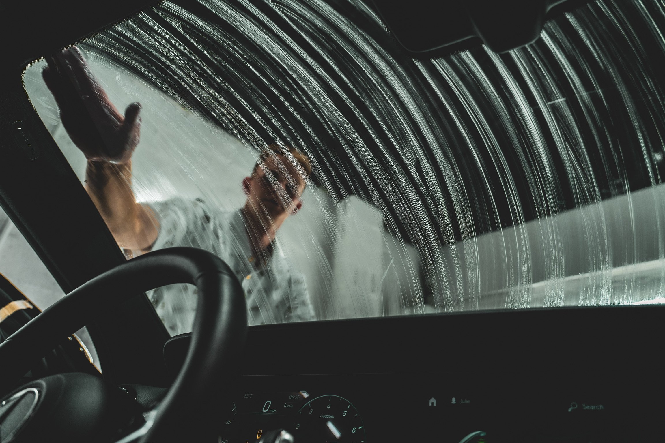 Person cleaning the inside of a car windshield with soap or cleaning solution, with soap streaks visible on the glass.