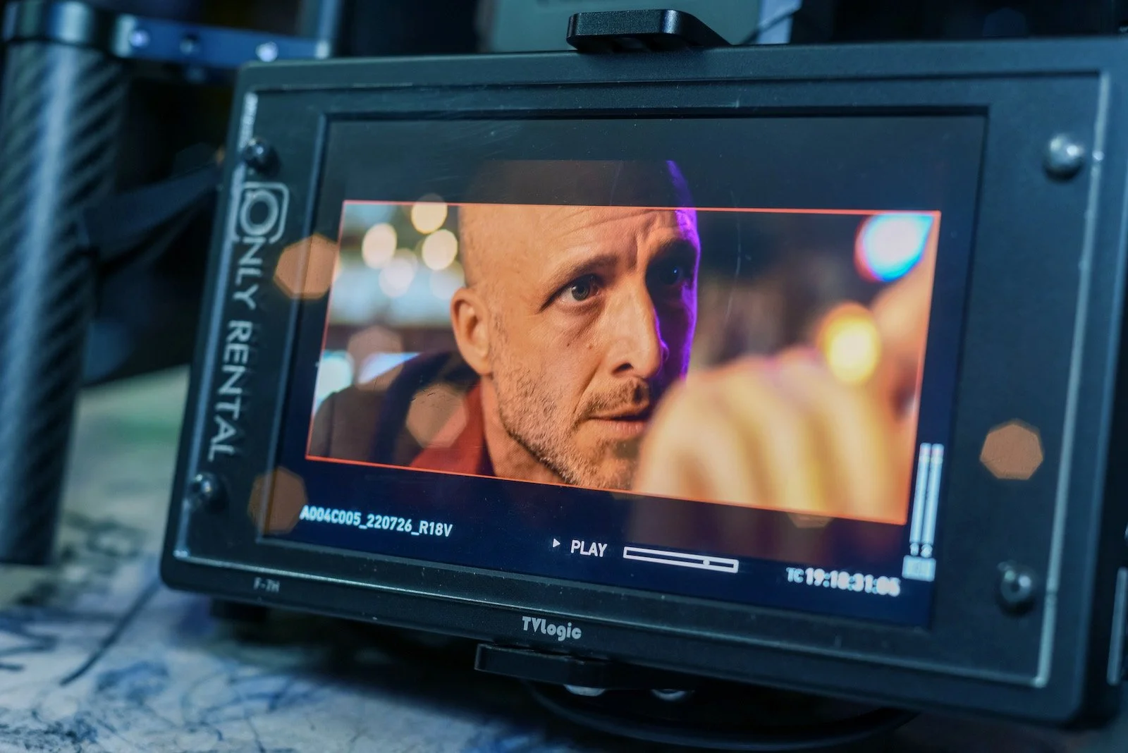 Close-up of a monitor showing a Tonic movie scene of actor Jason Coviello looking intensely at actor Billy Blair with blurred lights in the background.
