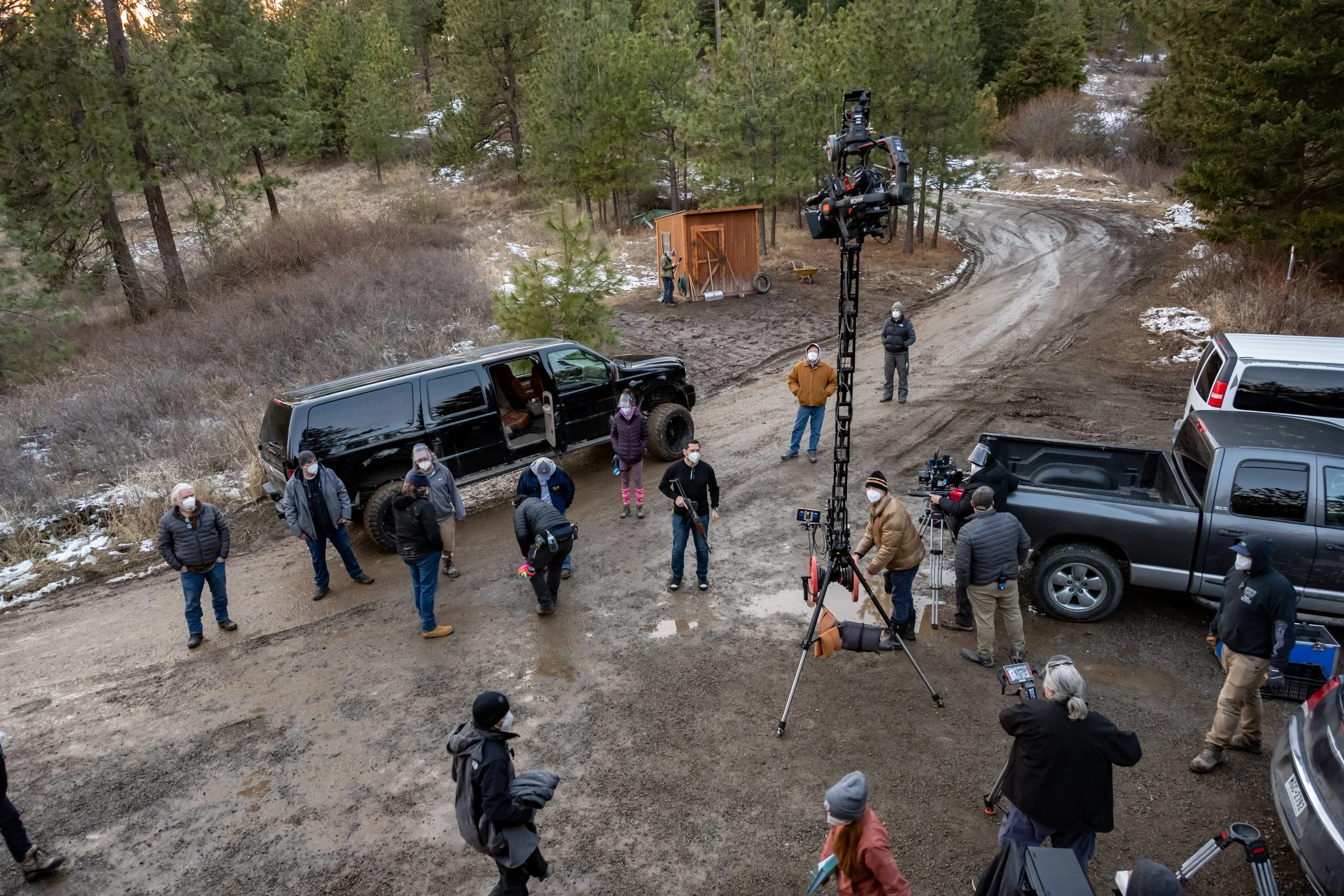 A film crew on a dirt road in a forest setting, with camera equipment and crew members wearing masks preparing for a shoot.