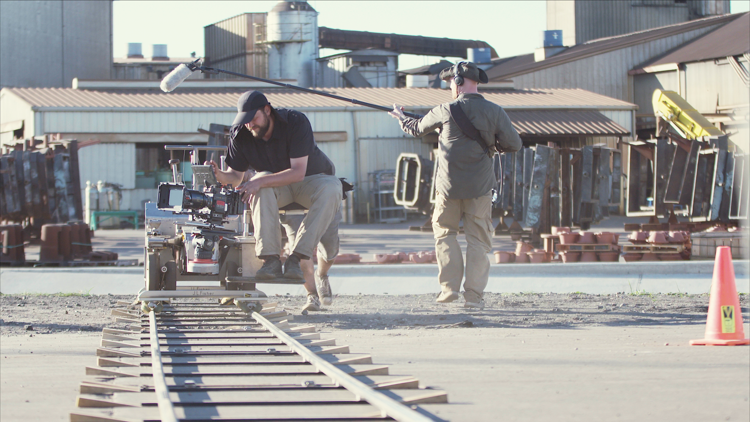 Filmmakers filming on outdoor railway tracks with camera and sound equipment, in an industrial area.