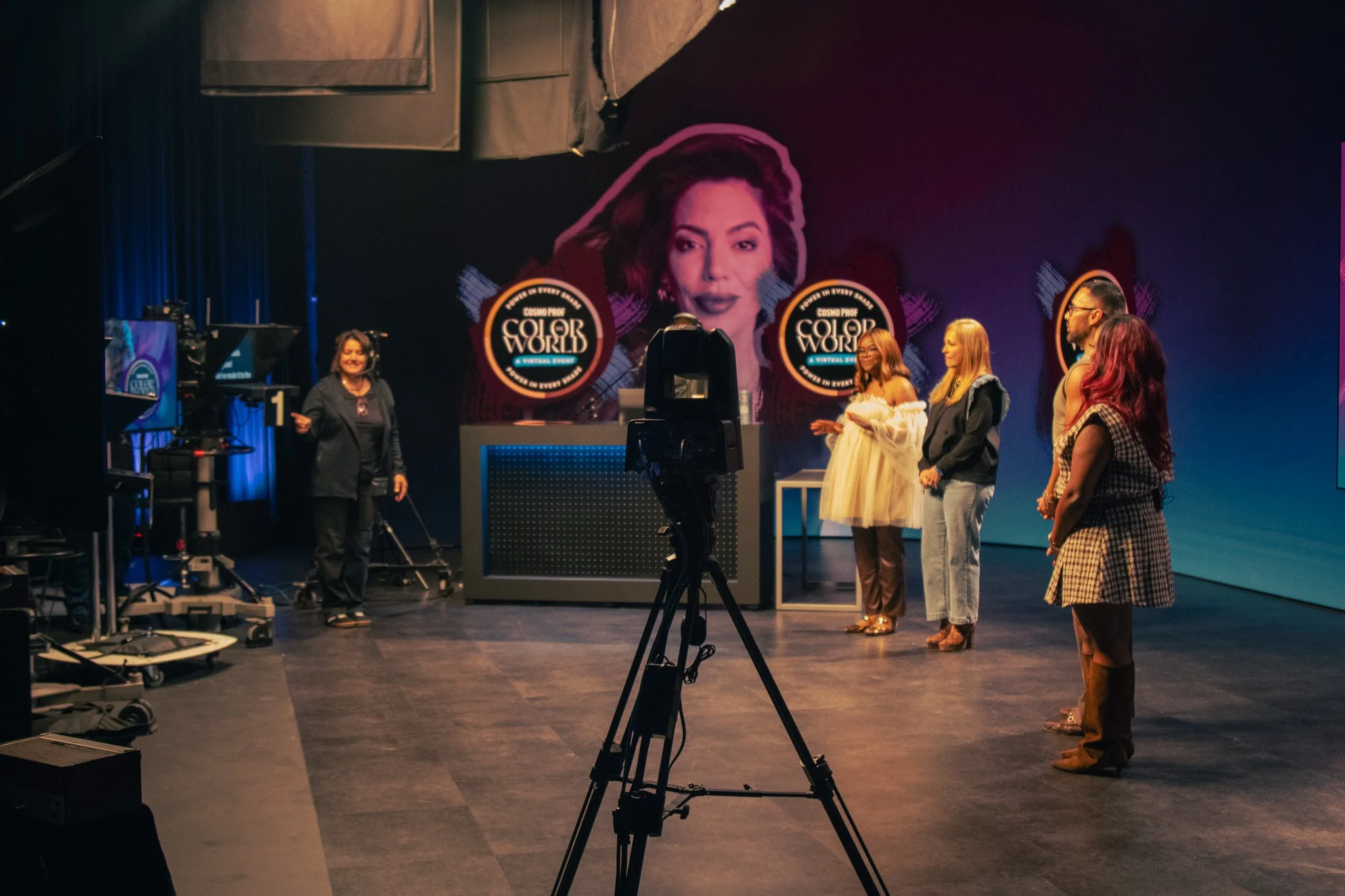 People on stage at a virtual event with a large banner displaying a woman’s face and the logo for 'Color World' in the background.