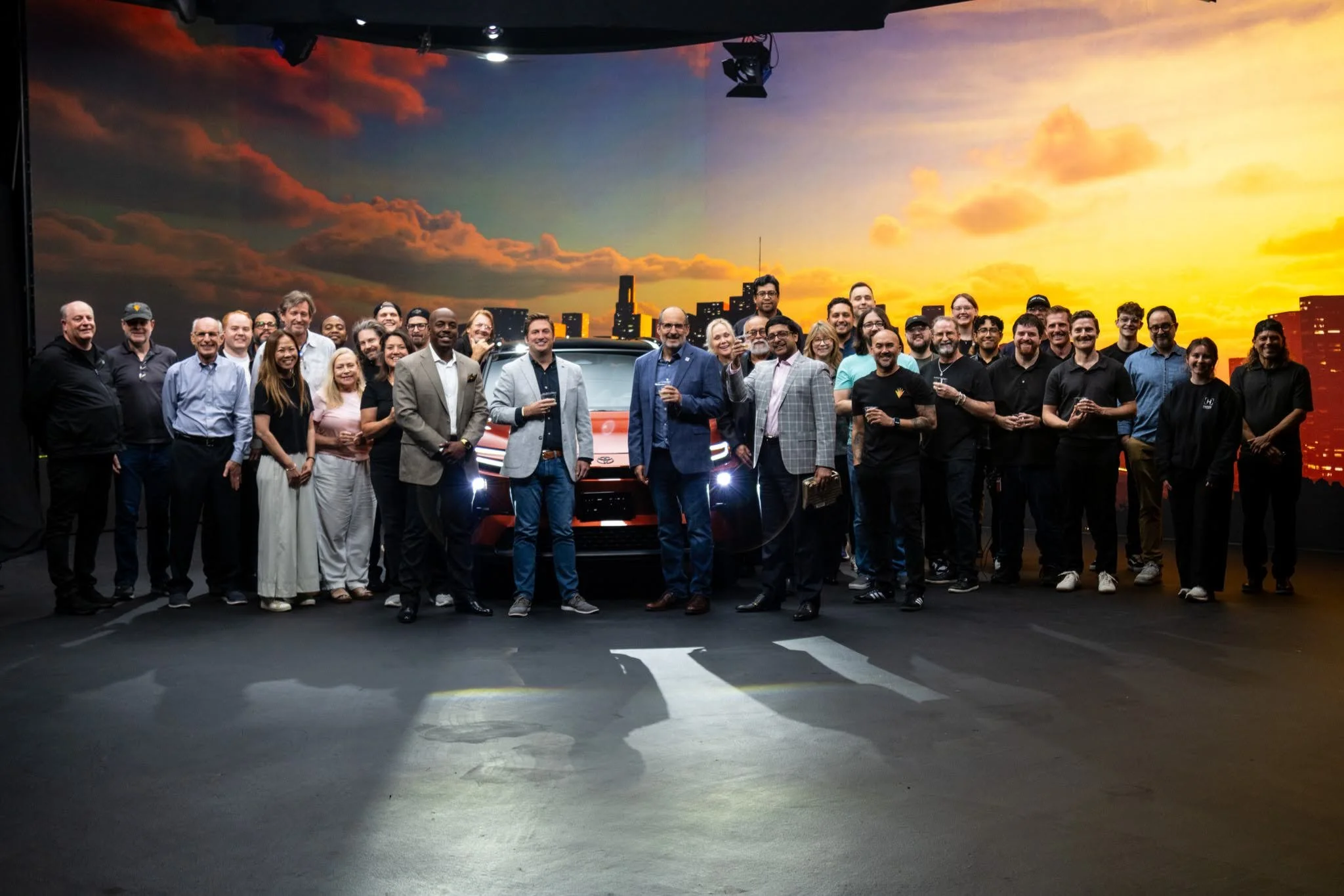 Crew on a shoot for a Toyota production gathered for a photo at AMS Pictures with a sunset cityscape background and a car in the background.