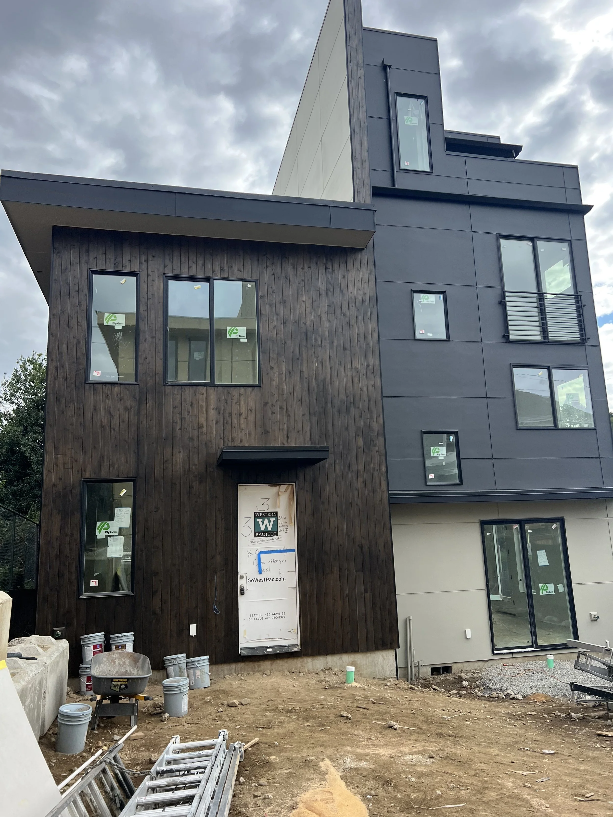 Under construction modern multi-story building with dark wood and black exterior, large windows, and a sliding glass door.