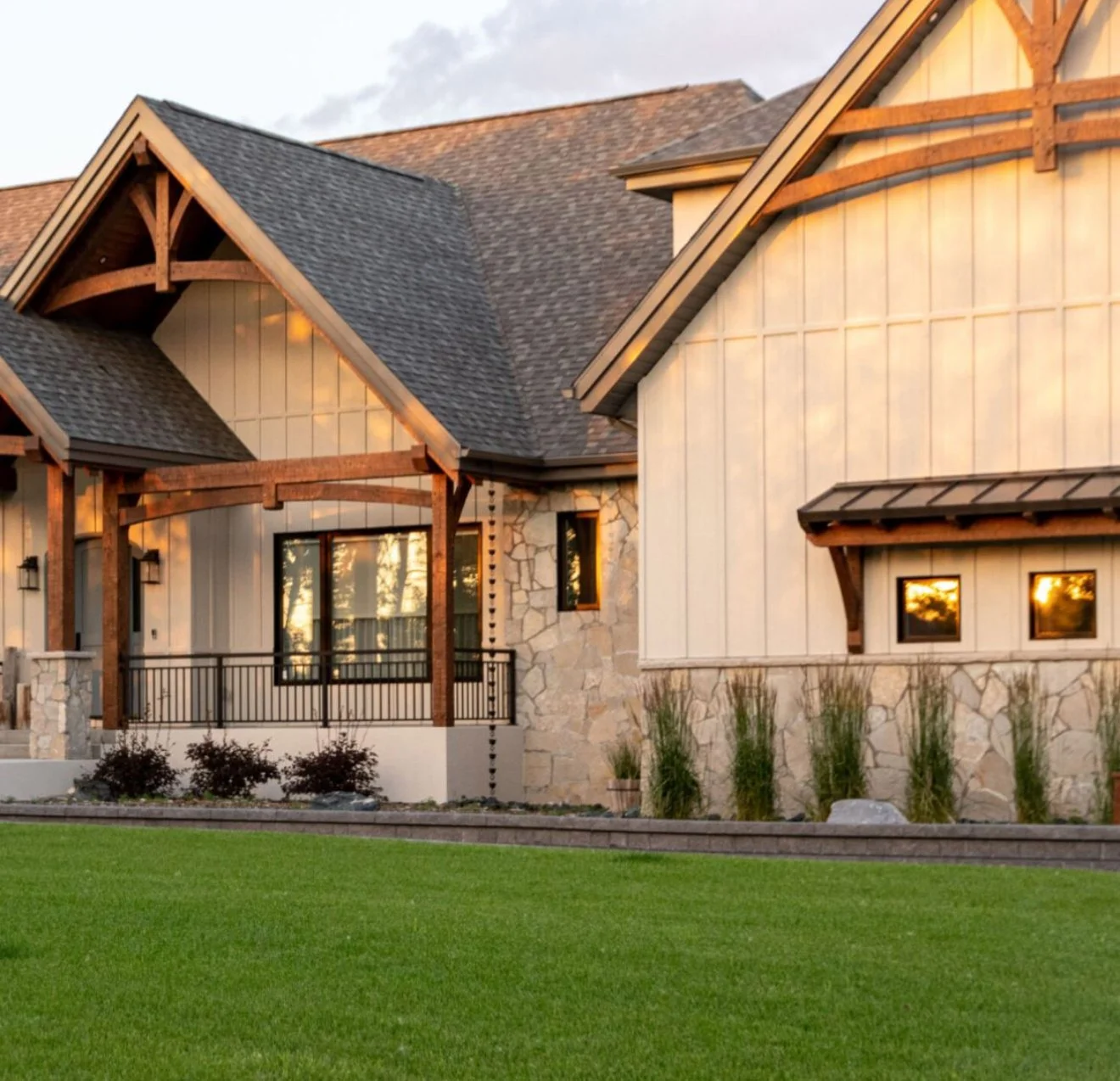 Exterior of a house with a combination of stone and wooden siding, a gabled roof, and a balcony with black railing at sunset.