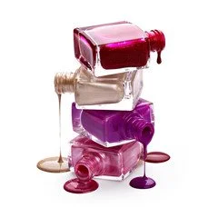 Stack of four nail polish bottles with spilled polish around them in various shades of pink, purple, and beige.