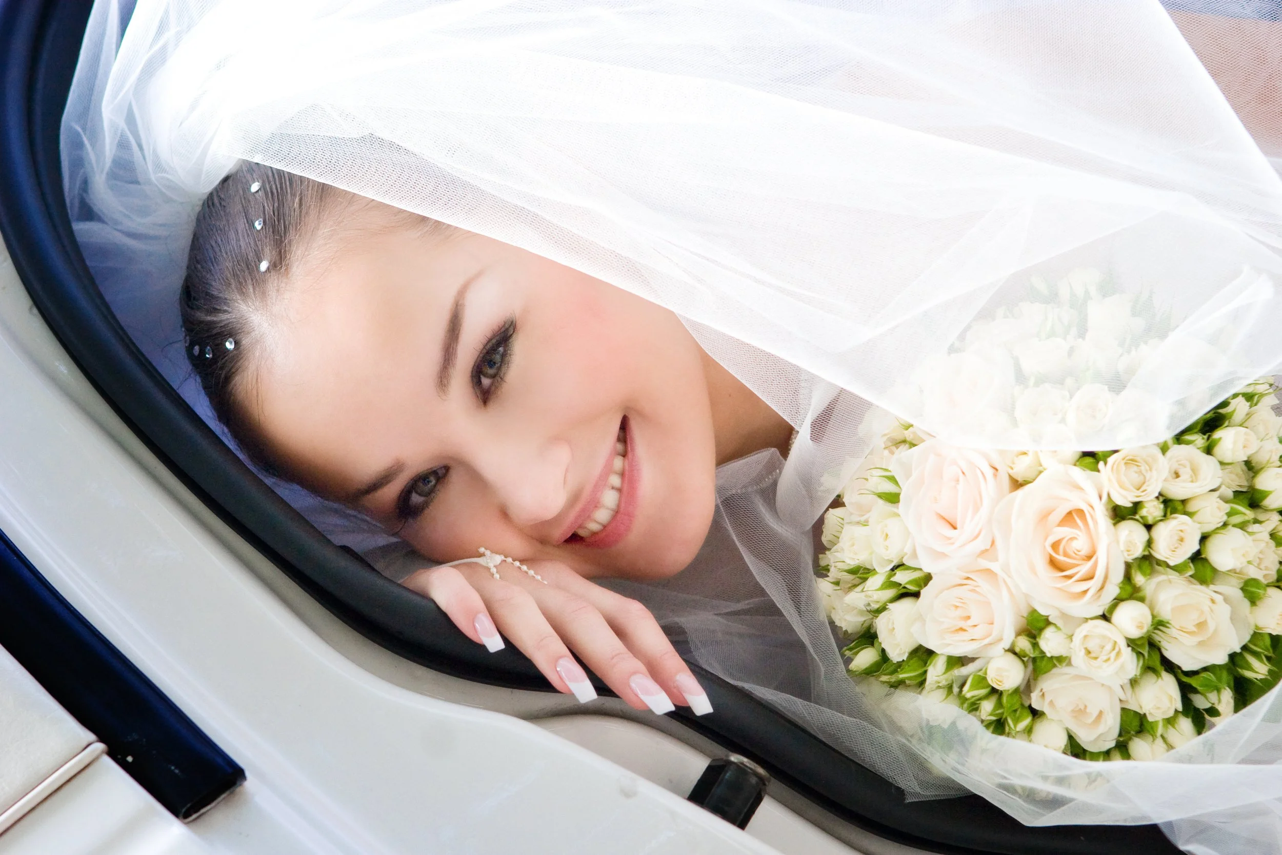 Smiling woman in wedding dress lying in car with flowers