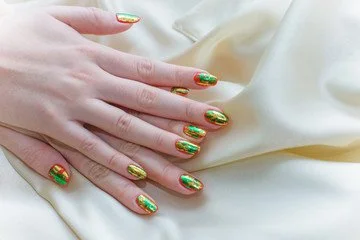 Hand with metallic green and red holiday-themed nail polish resting on white fabric.
