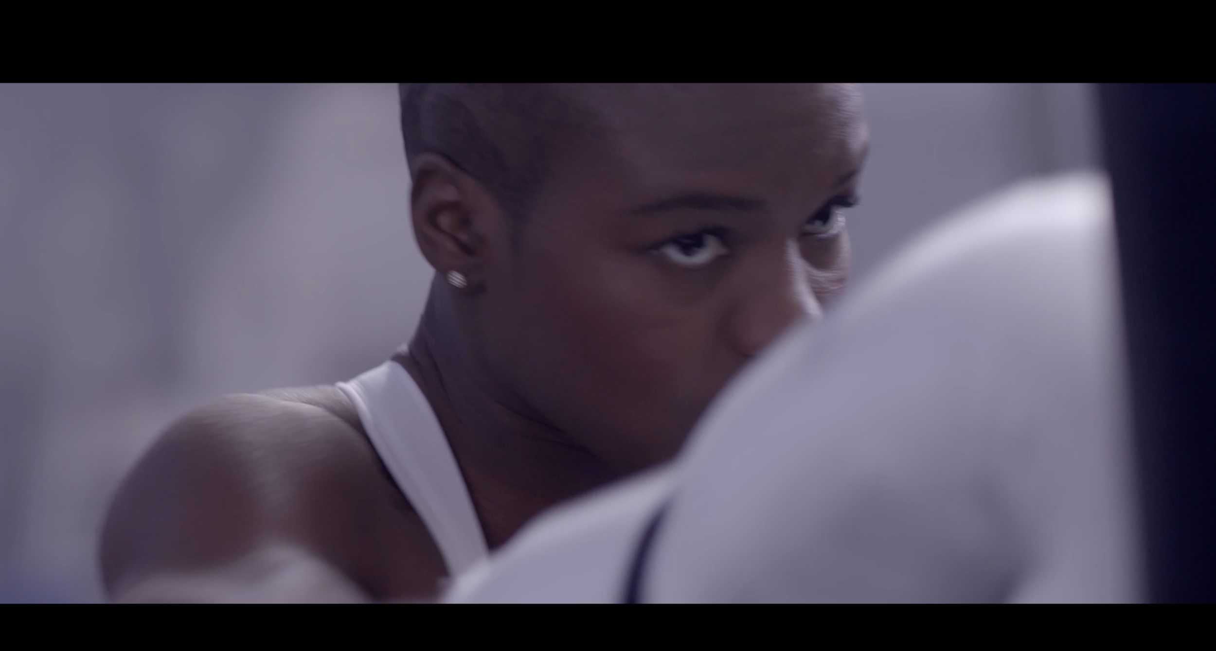 Nicola Adams, focused and looking over her shoulder, wearing a workout top in a gym or training environment.