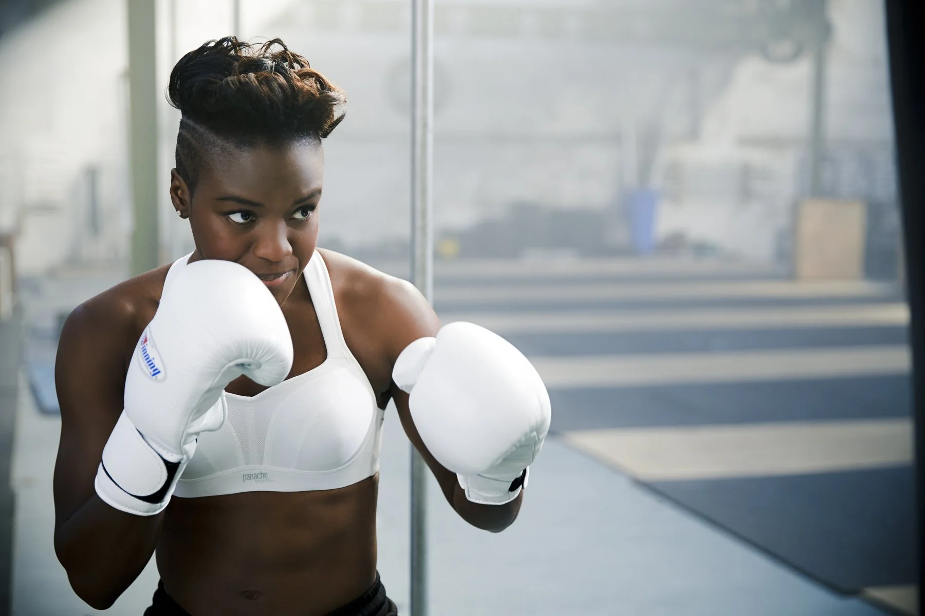 Nicola Adams in a gym, wearing boxing gloves and a white sports bra, practicing boxing punches.