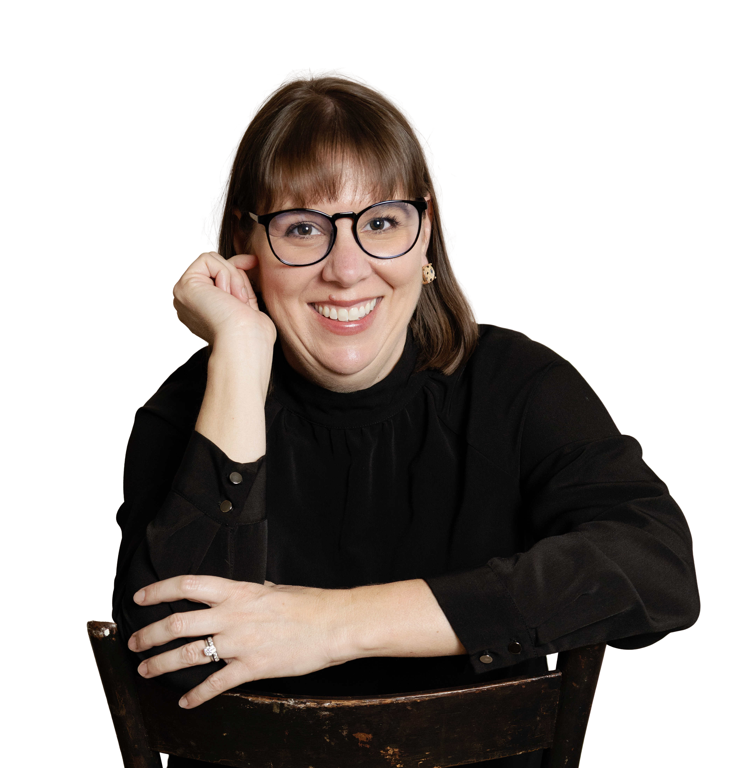 A woman smiling, wearing glasses, with her hair styled in a shoulder-length cut, and a black top, sitting with crossed arms.