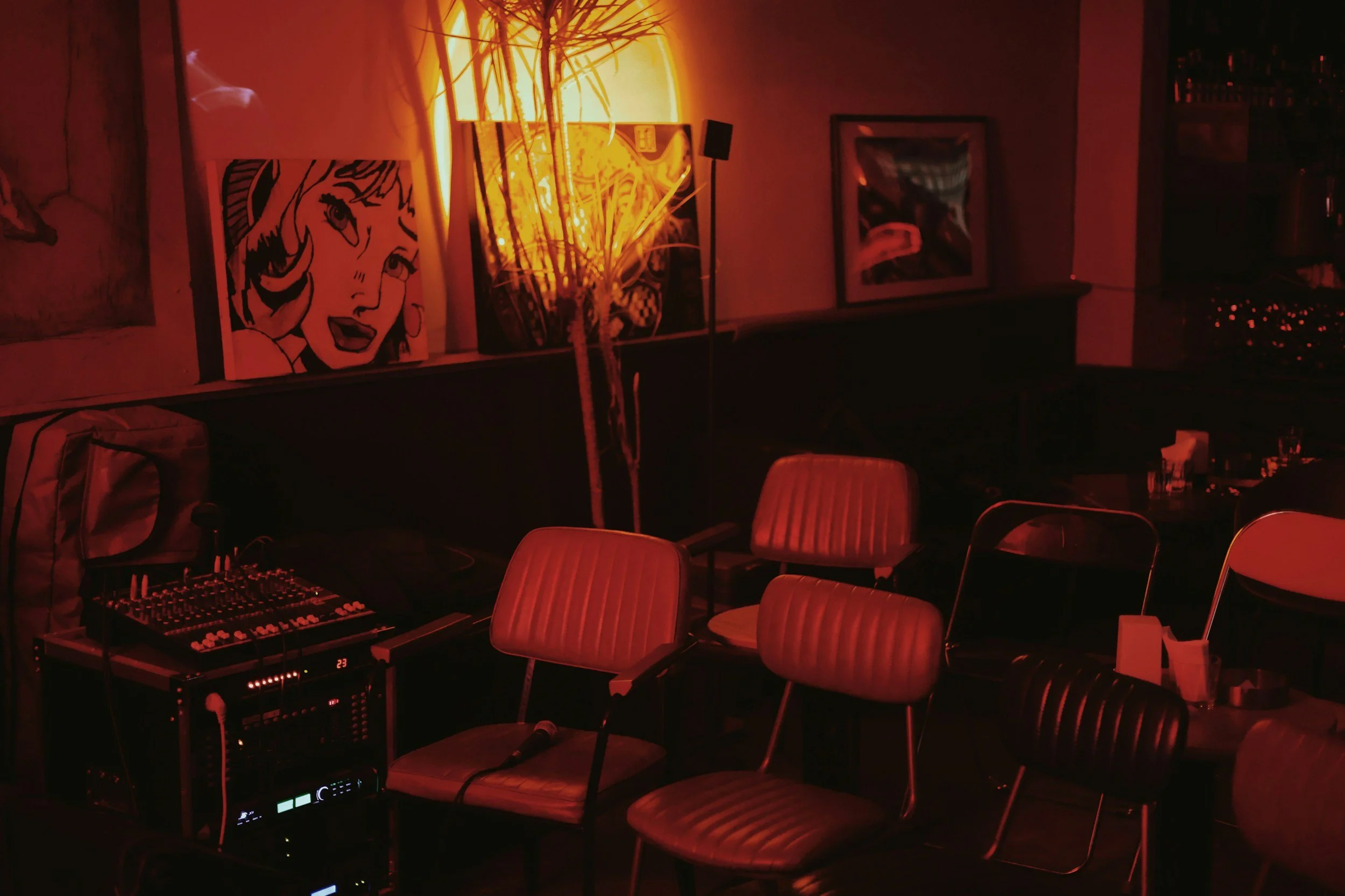 Empty bar or lounge area with red lighting, featuring chairs, a sound mixer, and artwork on the wall.