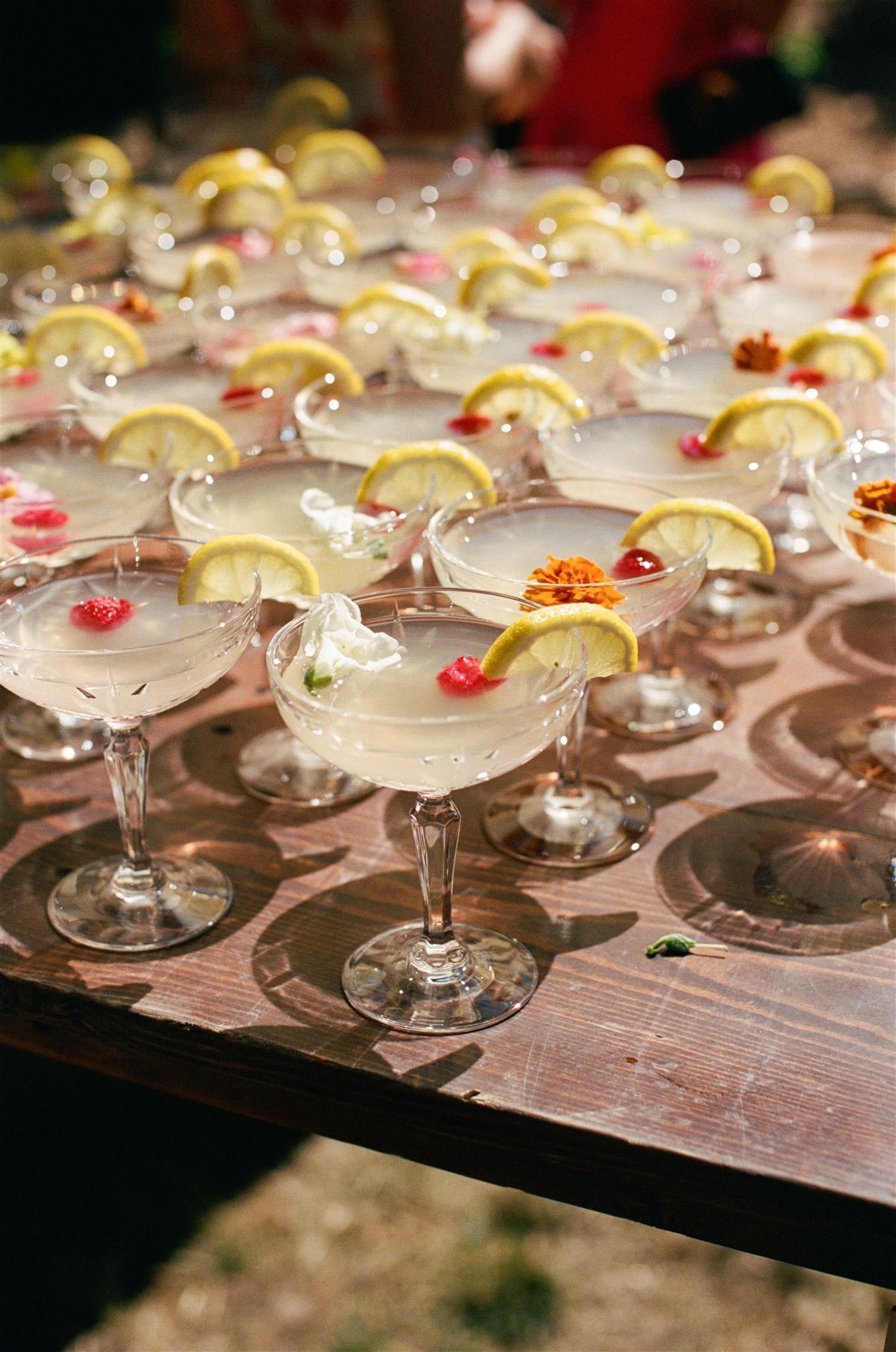 Multiple cocktails with lemon garnishes on a wooden table.