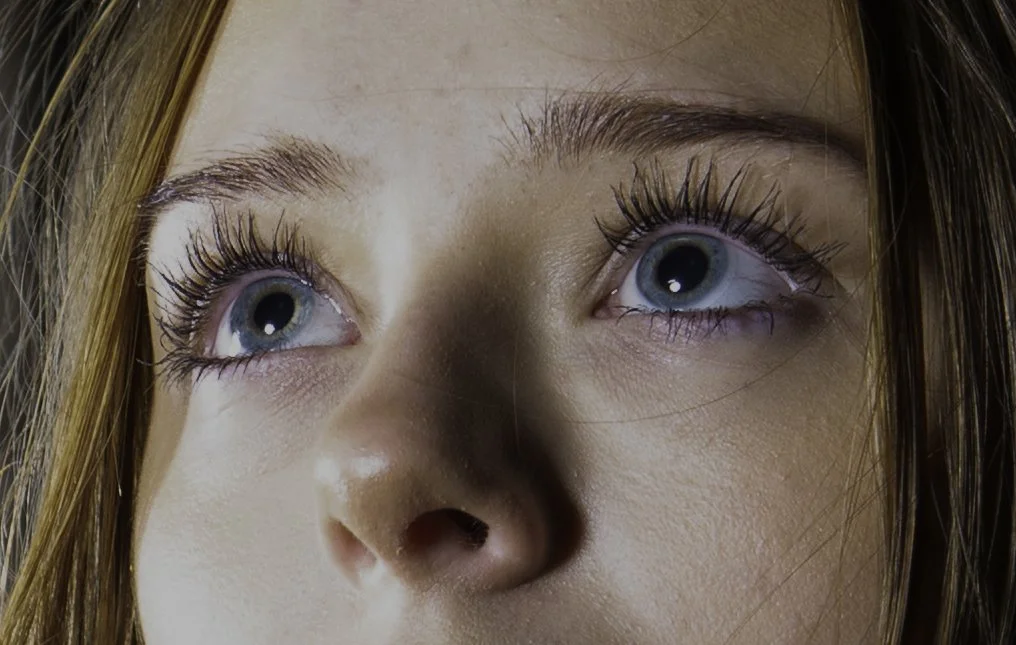 Close-up of a woman with blue eyes looking upward, showing her eyelashes and eyebrows.