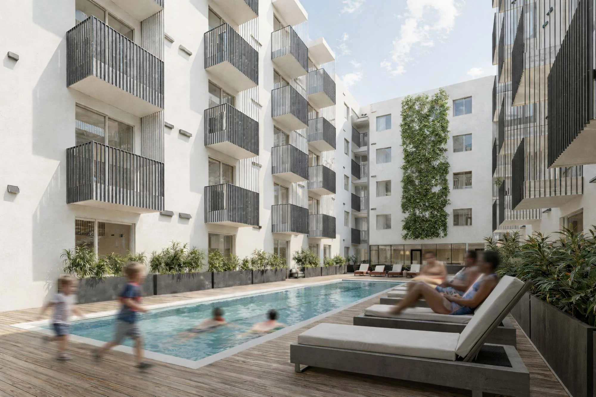 People relaxing on lounge chairs and children playing in a swimming pool at an apartment complex courtyard with modern white buildings, black railings, and a green vertical garden wall.