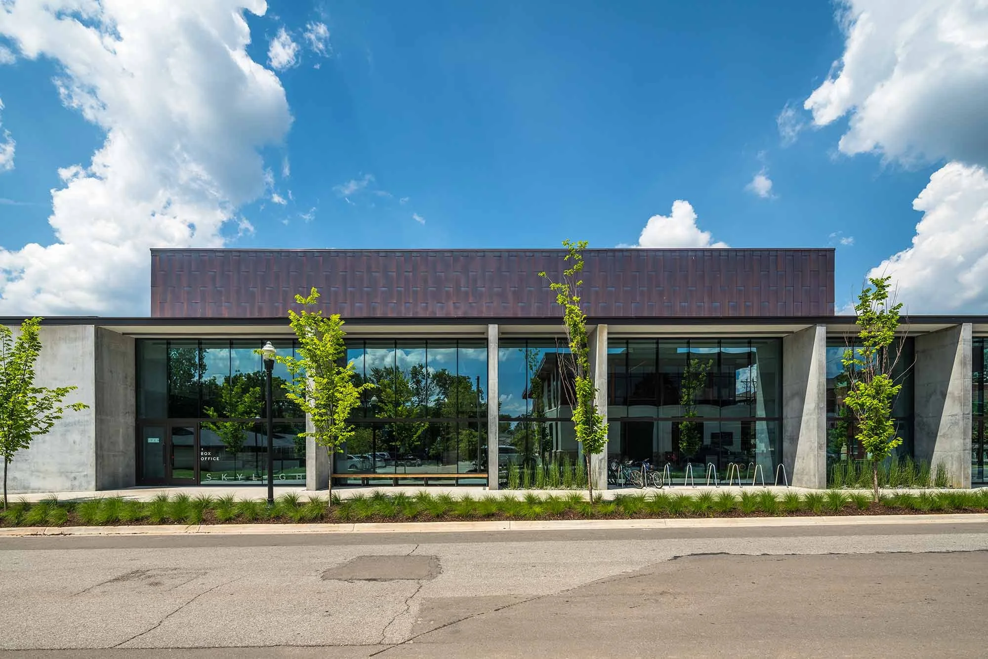 Modern building with large glass windows, trees in front, and a blue sky with clouds above.