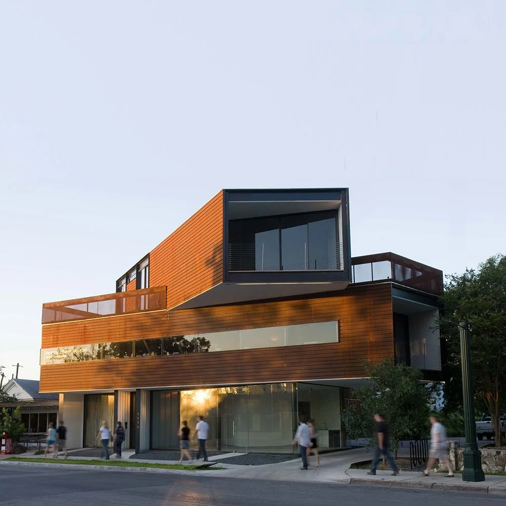 Modern multi-story building with glass windows and wooden exterior, people walking on the sidewalk in front, during sunset.