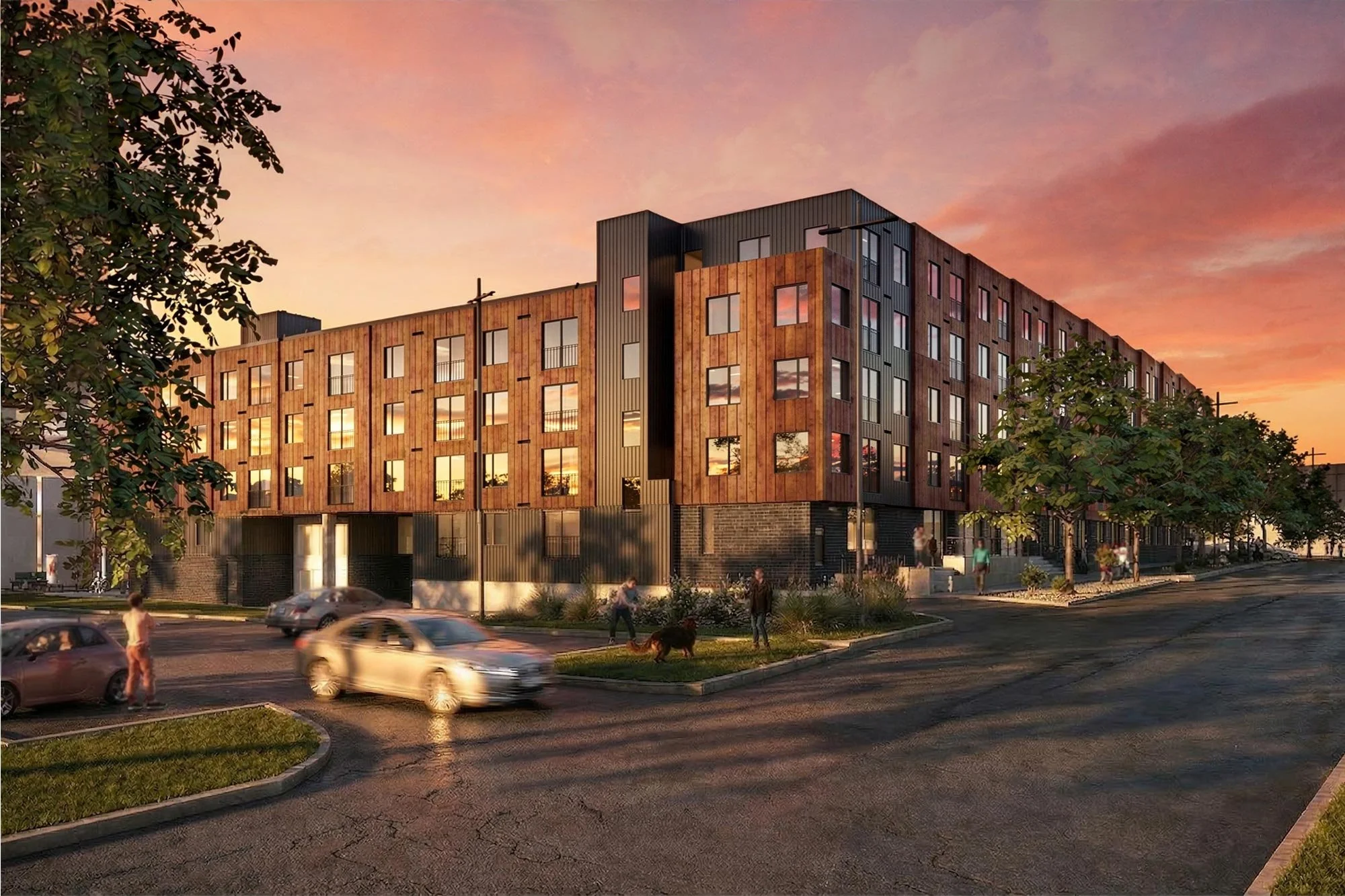 Modern multi-story apartment building with wooden and metal exterior, set against a sunset sky, with people walking dogs and cars driving by on the street.
