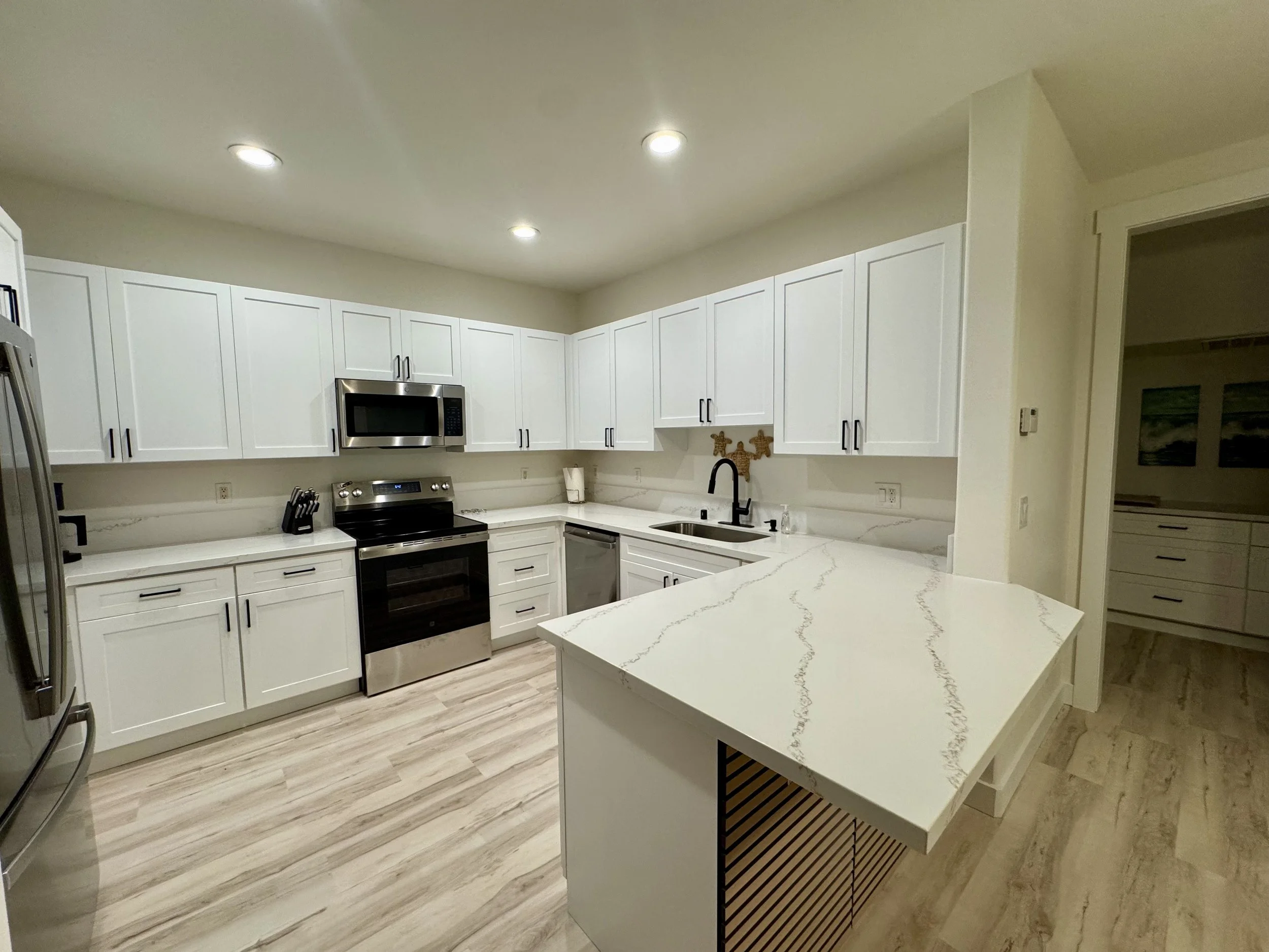 Modern kitchen with white cabinets, stainless steel appliances, and a marble countertop island. Recessed lighting and light wood flooring.