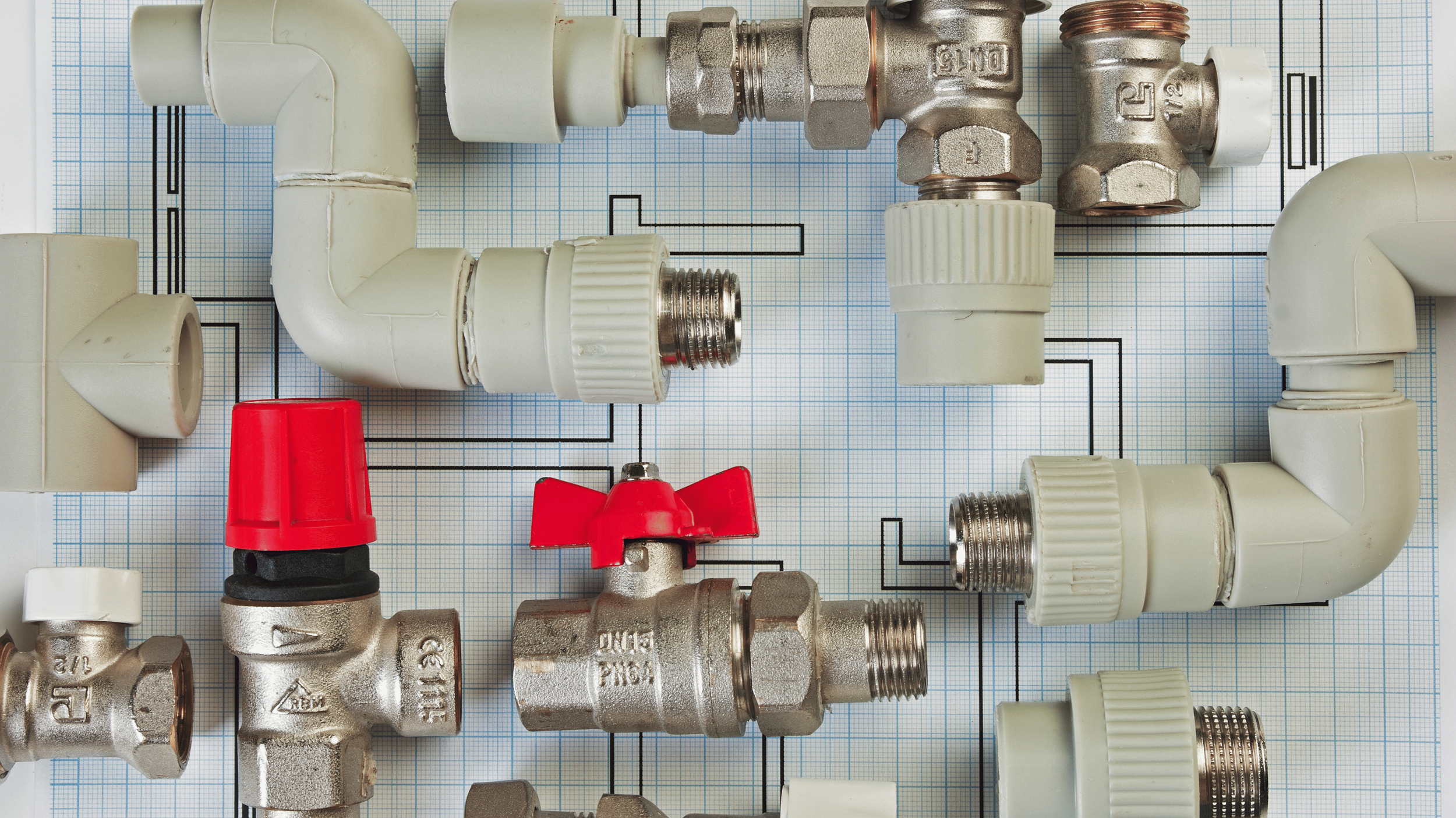 A plumbing diagram with various pipes, fittings, and valves arranged on graph paper. Includes PVC pipes, brass fittings, and a red valve handle.