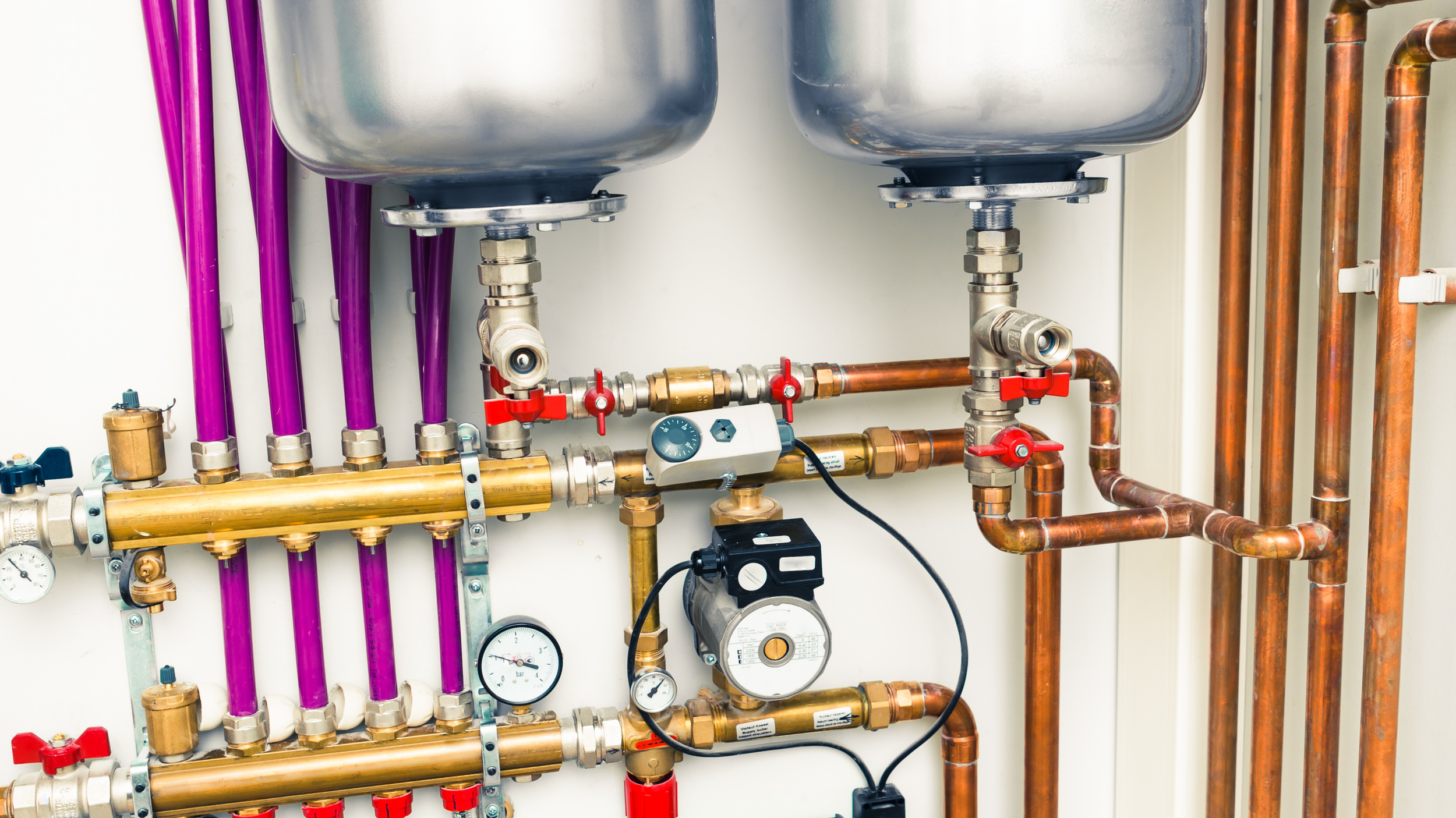 Close-up view of a plumbing system with copper pipes, purple PEX pipes, gauges, valves, and a pressure regulator.