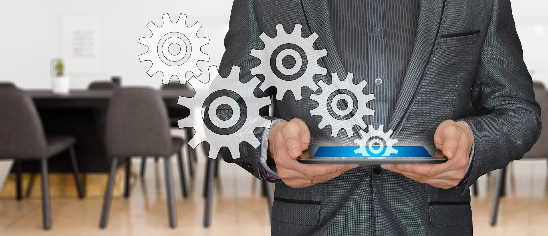 Businessperson in suit holding a tablet with gears overlay, symbolizing technology or process management, in a conference room.