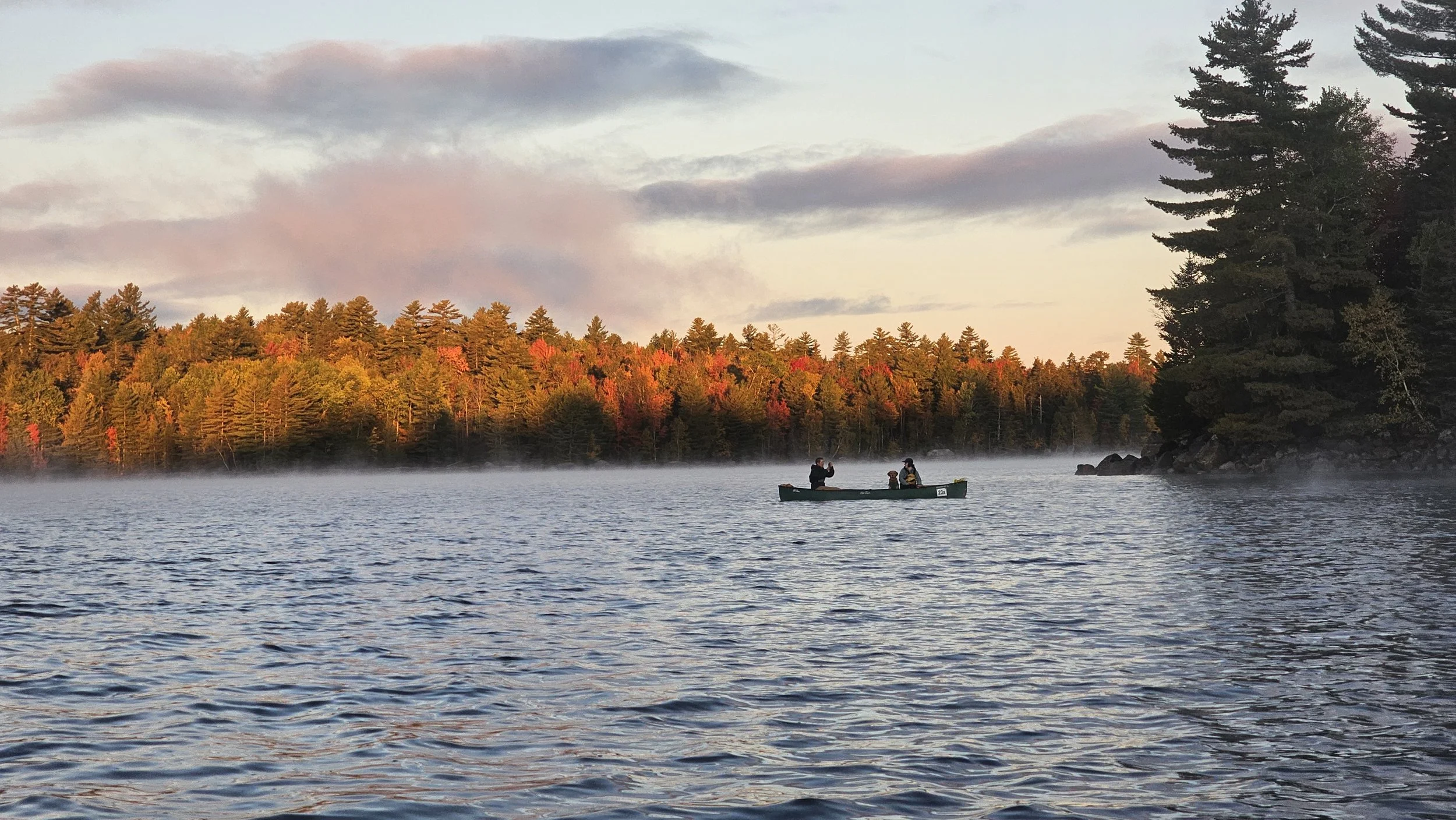 Two paddlers and a dog enjoy a sunrise canoe trip