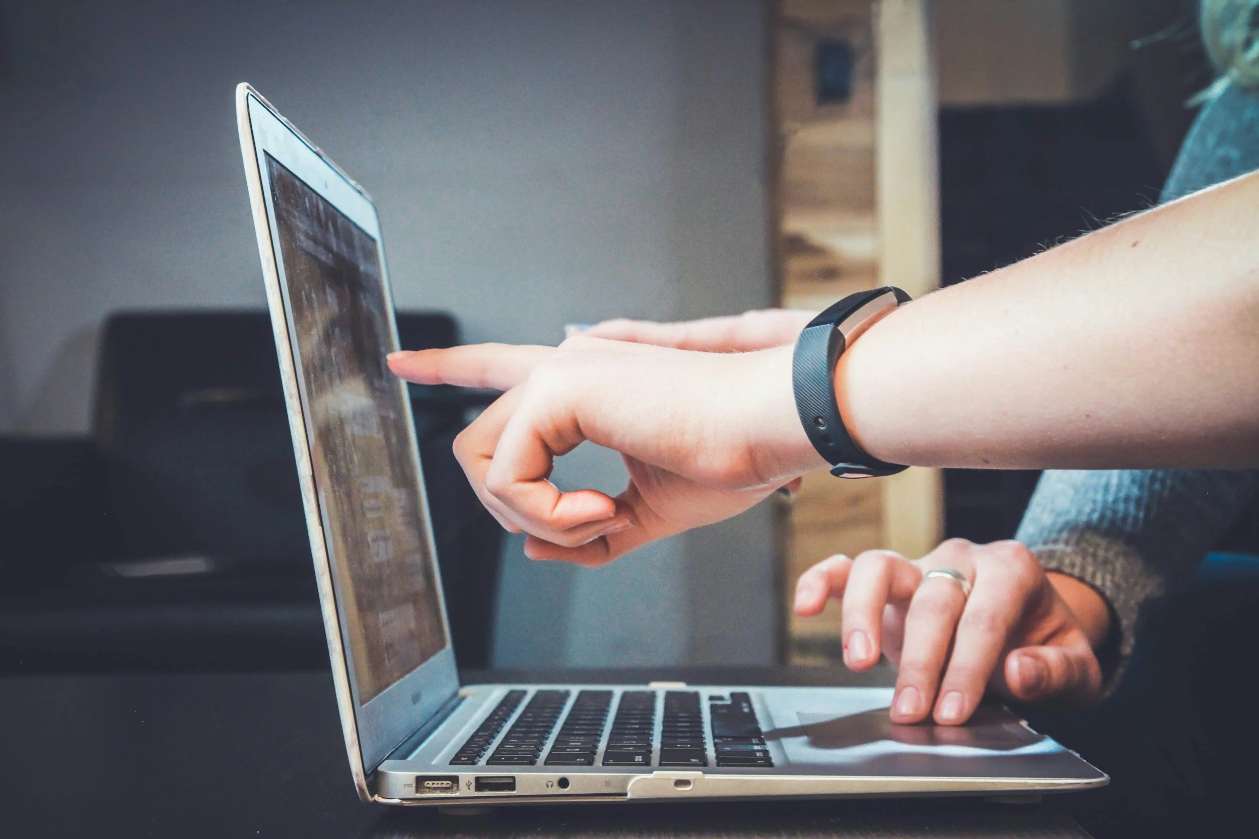 A person is using a laptop computer, with one hand extended to touch the screen and the other resting on the keyboard.