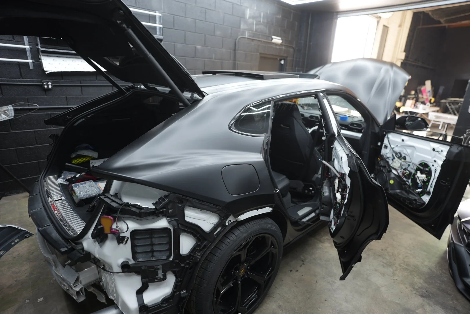 A white Lamborghini Urus disassembled and wrapped in 3M Satin black, with the front and rear interior panels removed and the hood open to wrap as much of the factory color as possible.
