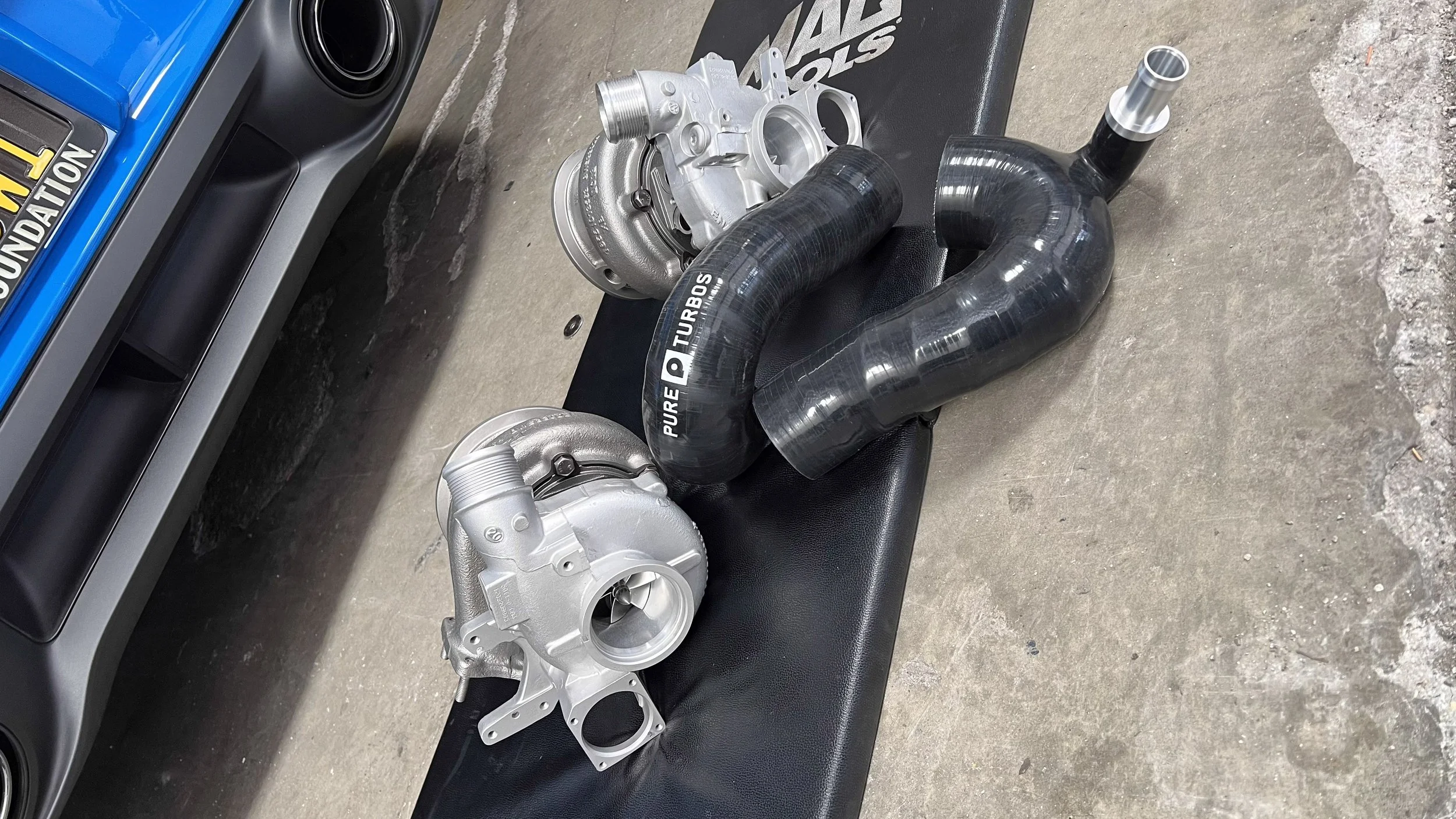 Upgraded PURE Turbos turbochargers and silicone hoses laid out beside a blue Porsche 911 Turbo S at Custom Luxury Lab in Frisco, TX