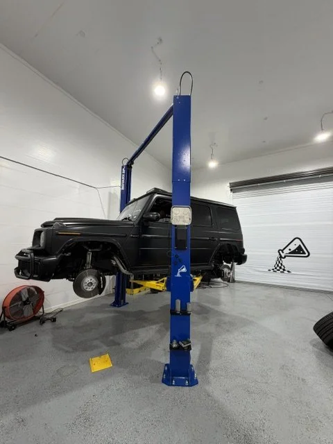 Black Mercedes-Benz G-Class raised on the two-post lift with a front wheel off at Custom Luxury Lab in Frisco, TX