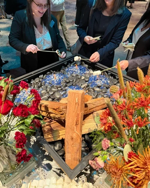 People gathered around a coal-themed display with rocks and logs, decorated with red and orange flowers.