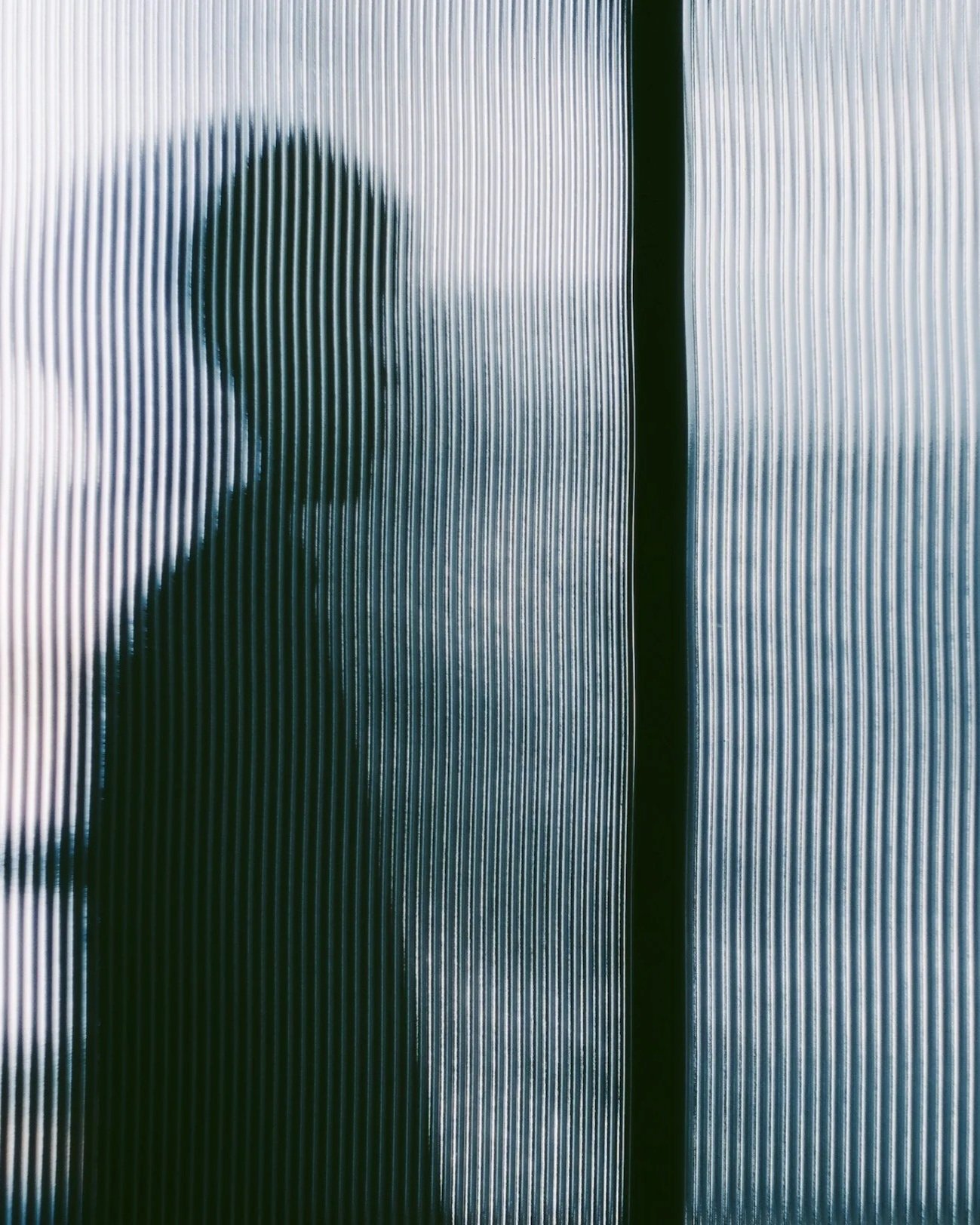 Silhouette of a person behind frosted glass with vertical line texture.