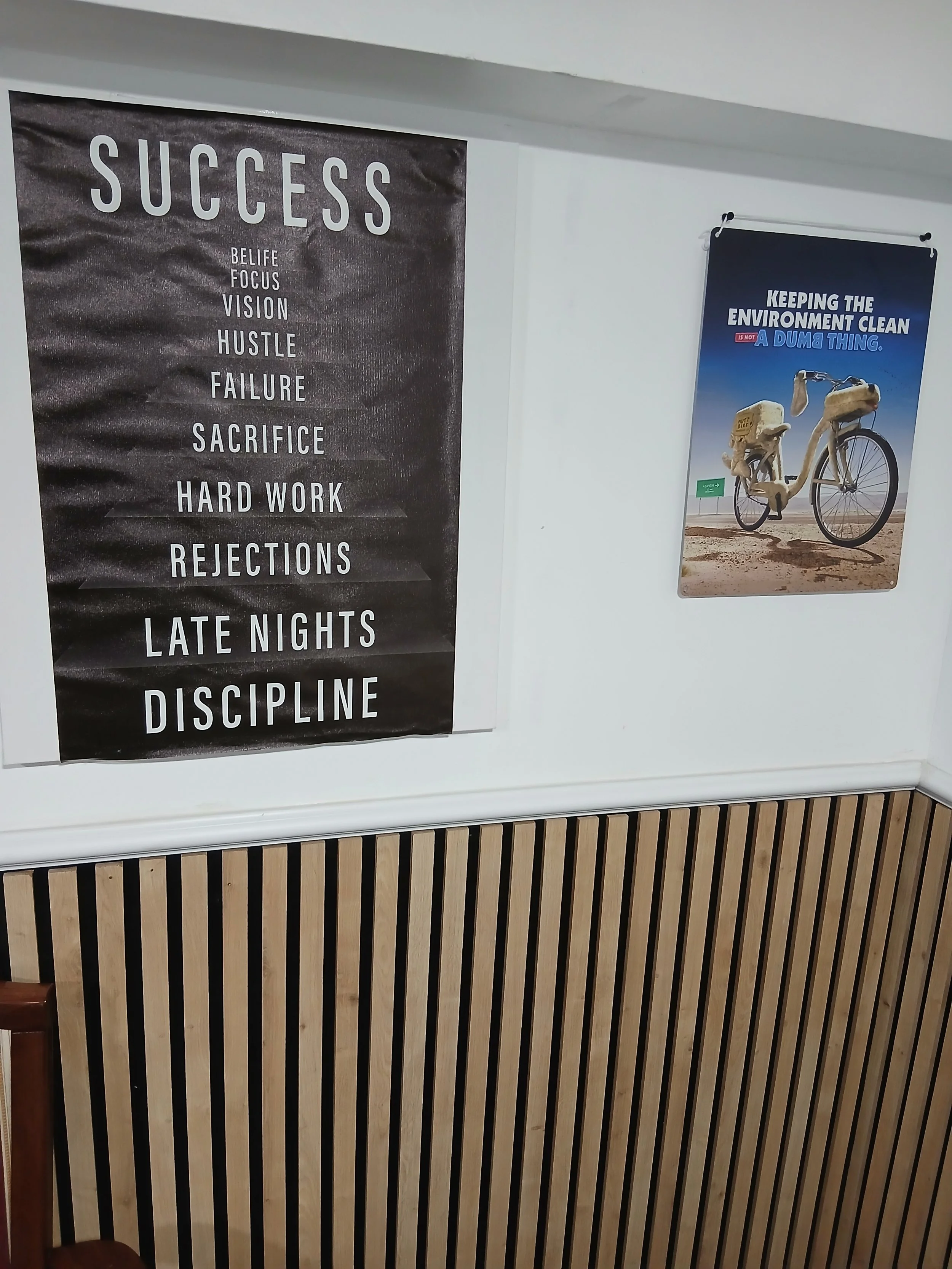 Posters on a wall with motivational messages and a bicycle image, including the words 'Success' and 'Keeping the environment clean is not a dumb thing.'