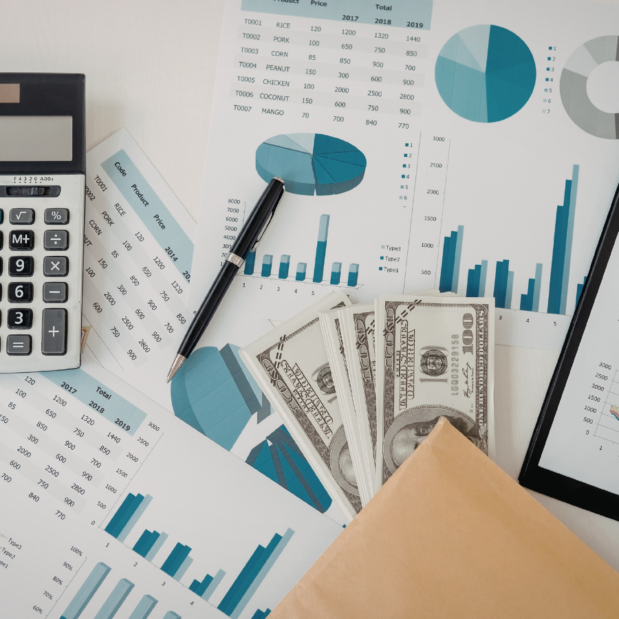 Financial documents with bar charts, pie charts, a calculator, a pen, US dollar bills, and an envelope on a desk.