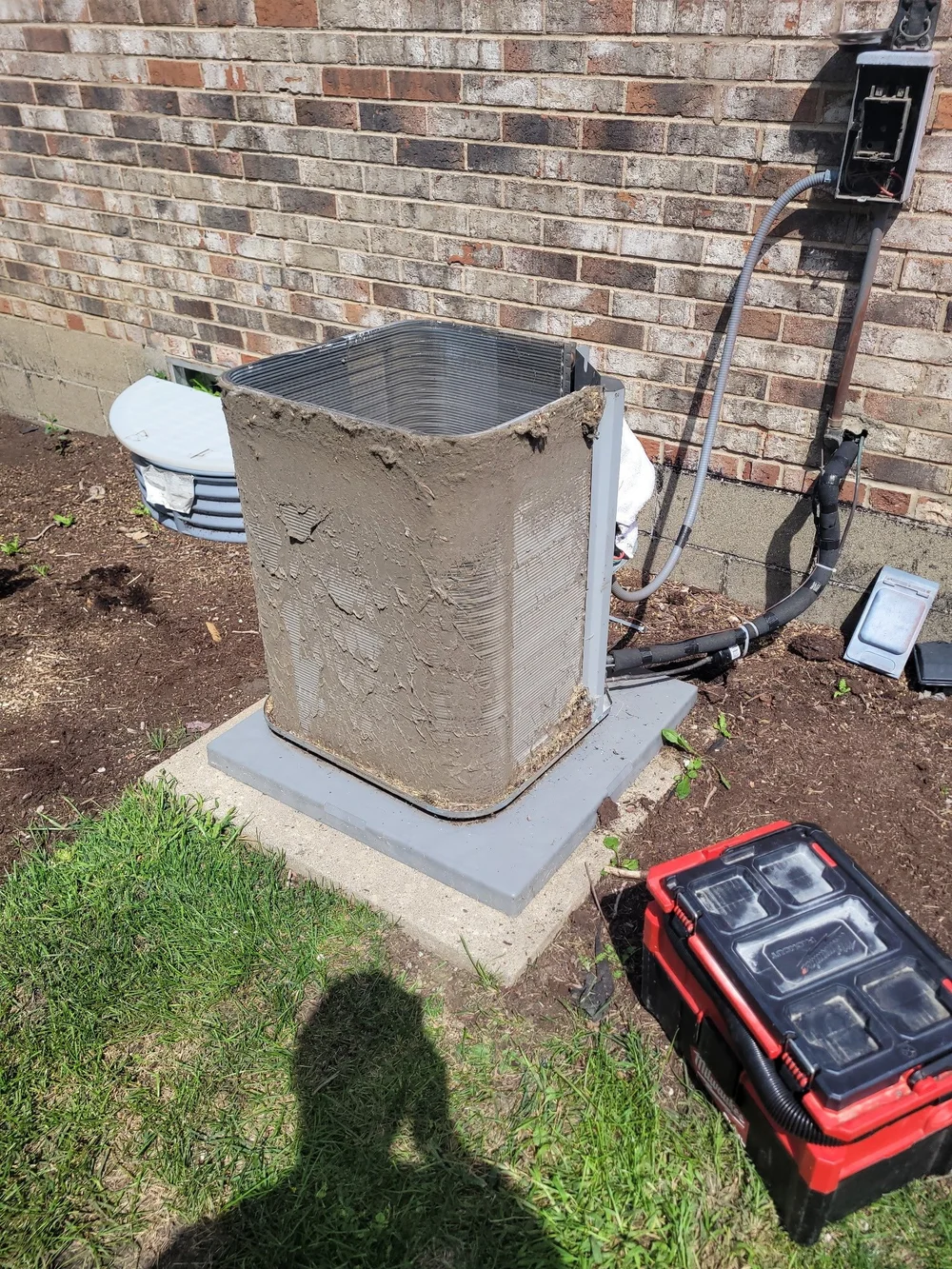 An outdoor condenser with its cabinet panels removed beside a brick wall.