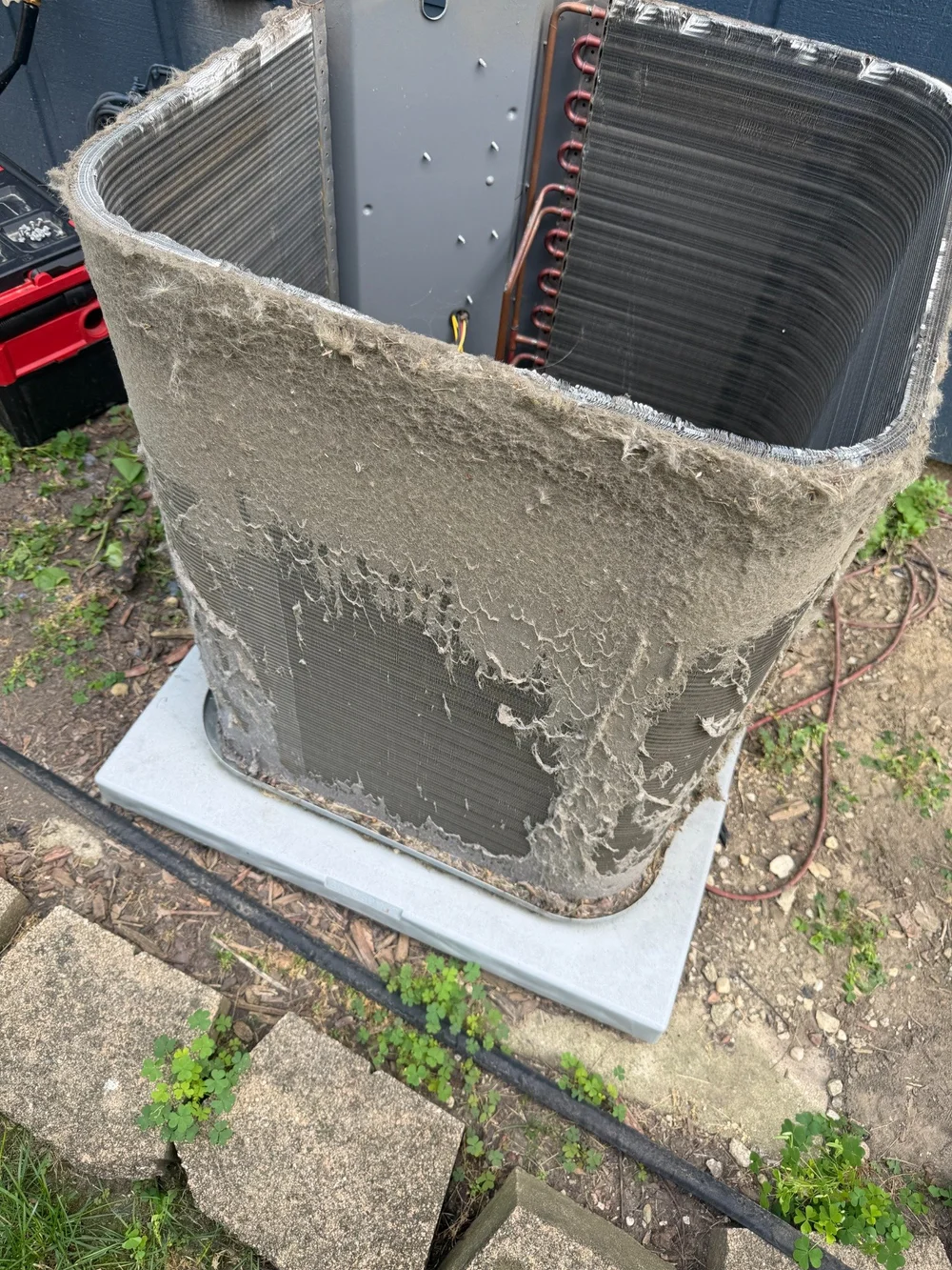 An exposed outdoor condenser coil with a visible mat of debris across the exterior fins.