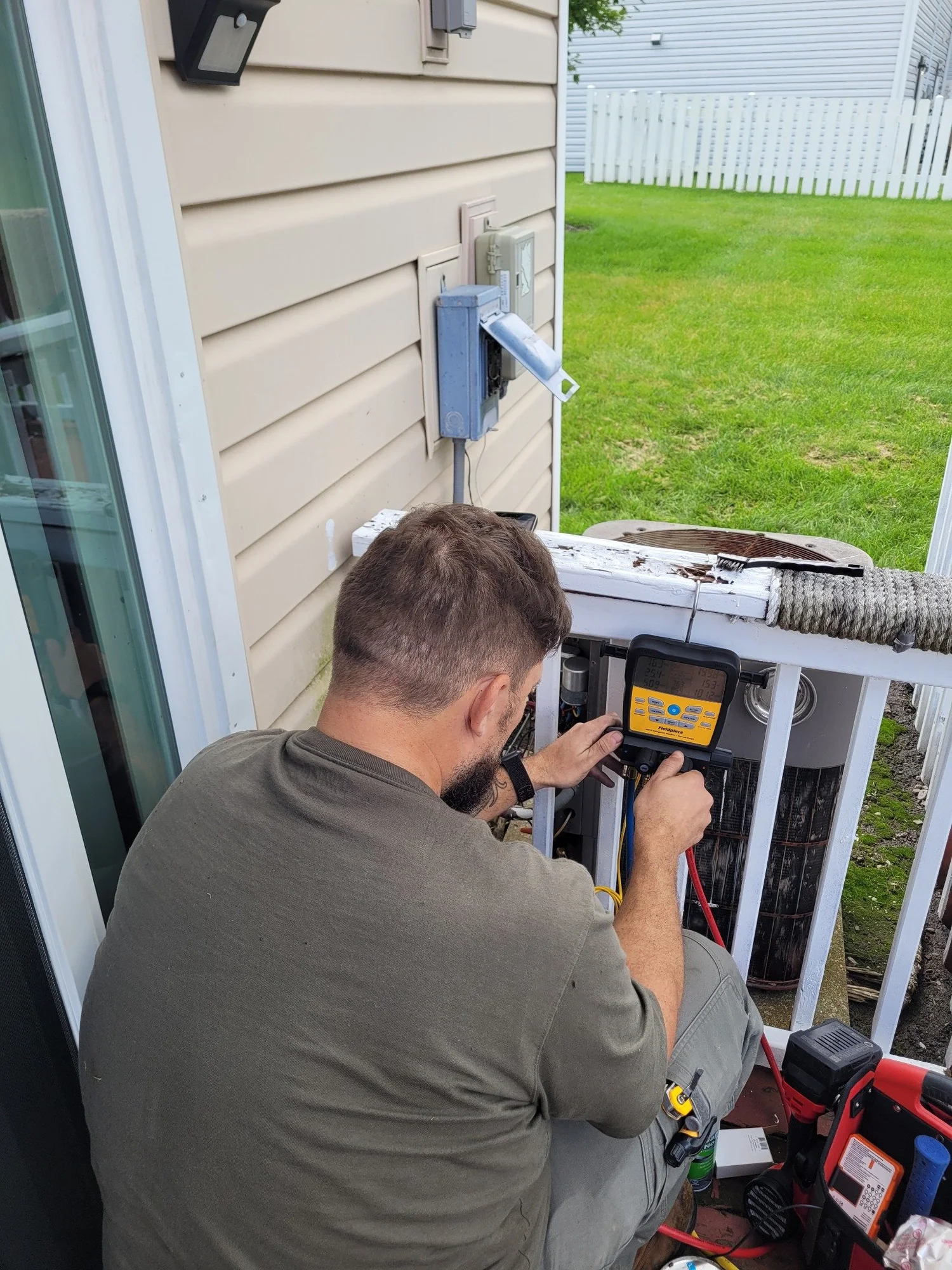 Technician checking a digital manifold during an outdoor HVAC service visit.
