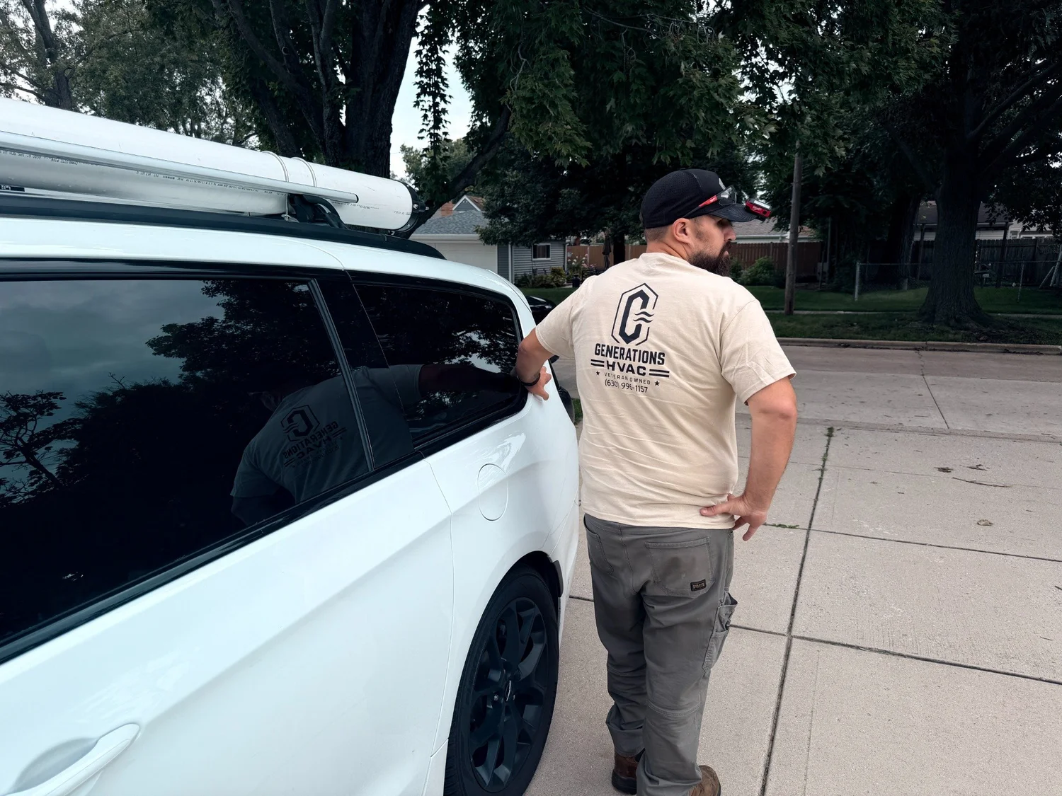 A Generations HVAC team member beside a white service vehicle in a residential neighborhood.