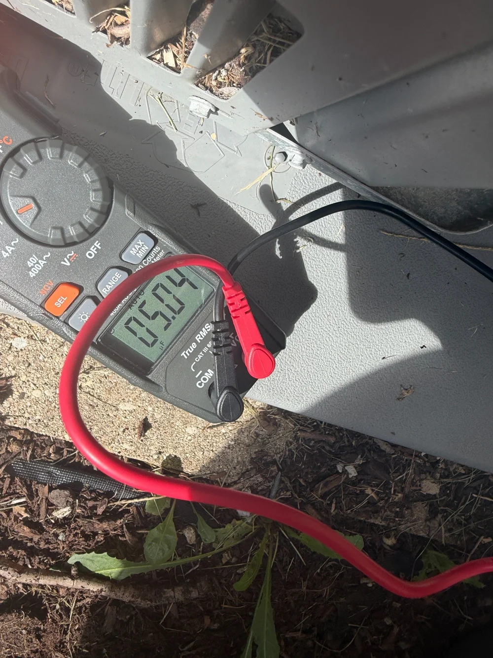 A digital meter and test leads during an HVAC capacitance measurement.