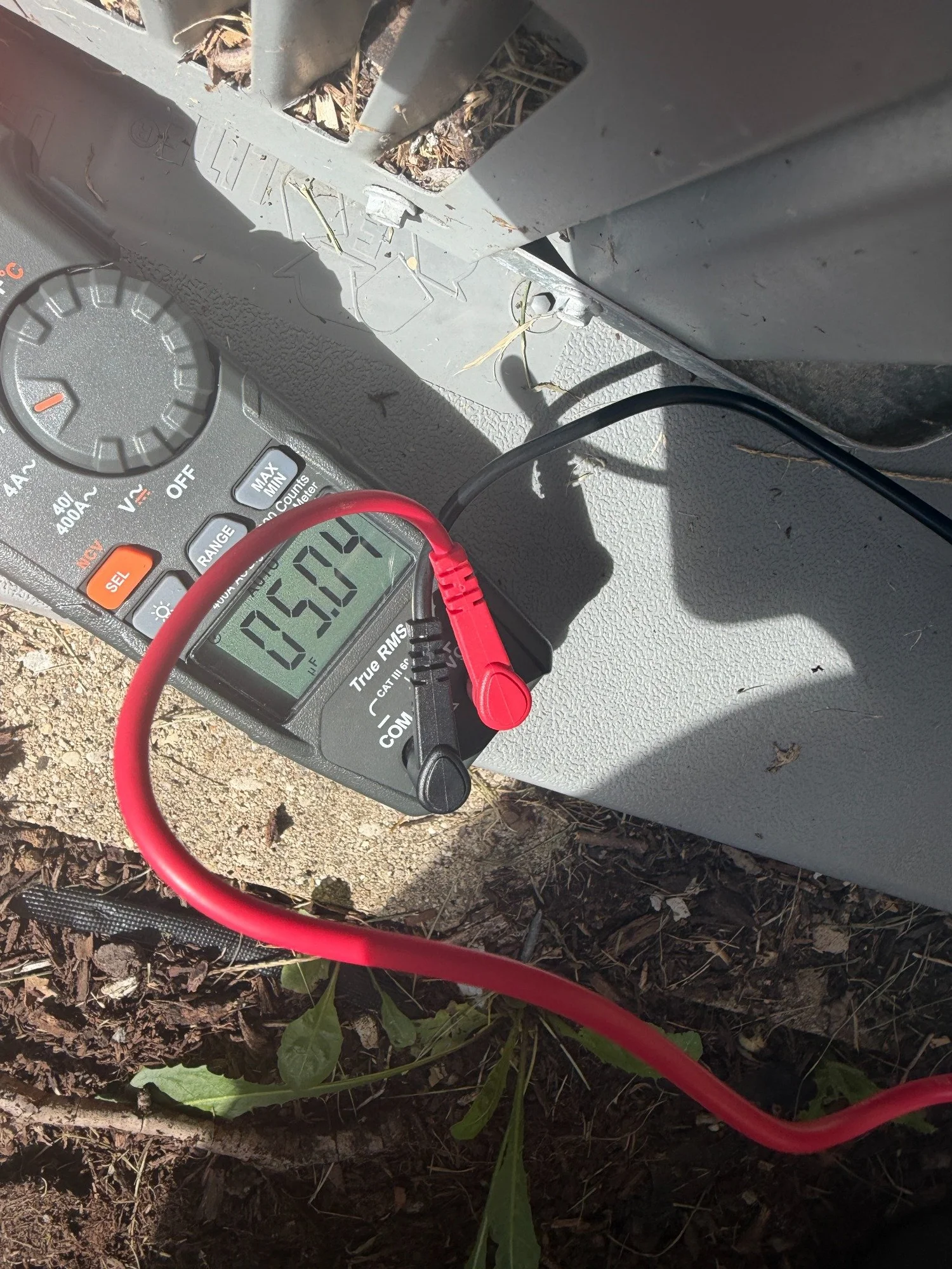 A digital meter during a capacitance measurement in an outdoor HVAC electrical compartment.