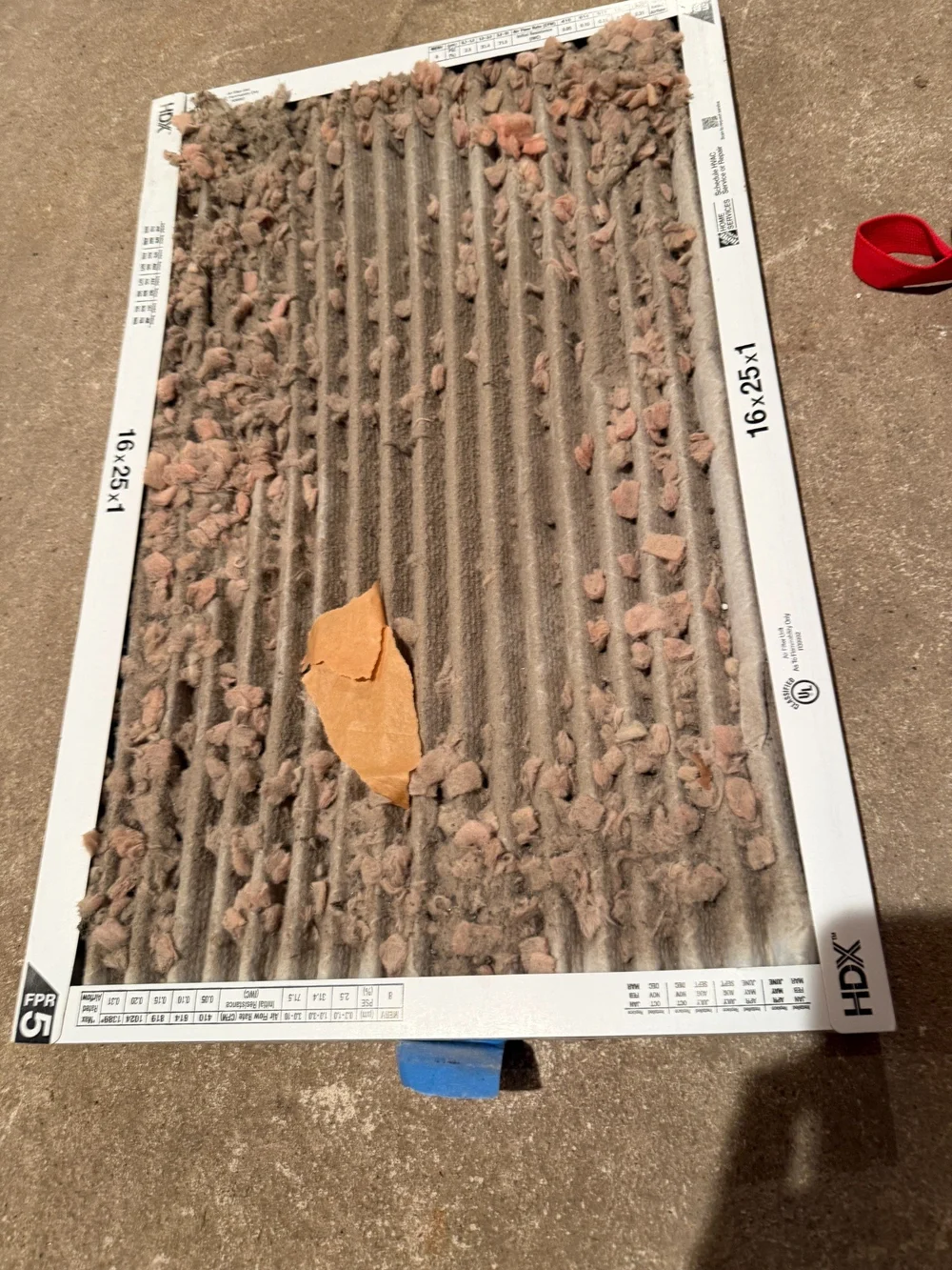 A used pleated HVAC filter with visible debris, lying on a concrete floor.
