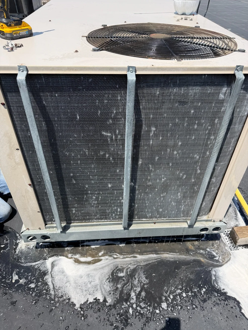 An exposed outdoor condenser coil during cleaning, with wash water below the unit.