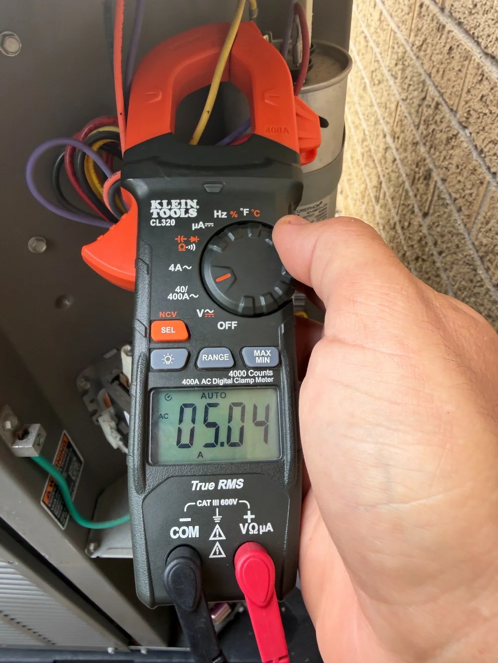 A technician using a clamp meter during an HVAC current measurement.