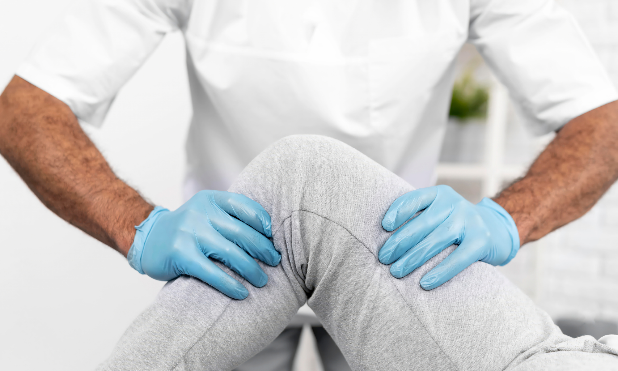 Person wearing a white medical coat and blue gloves holding someone's knee.
