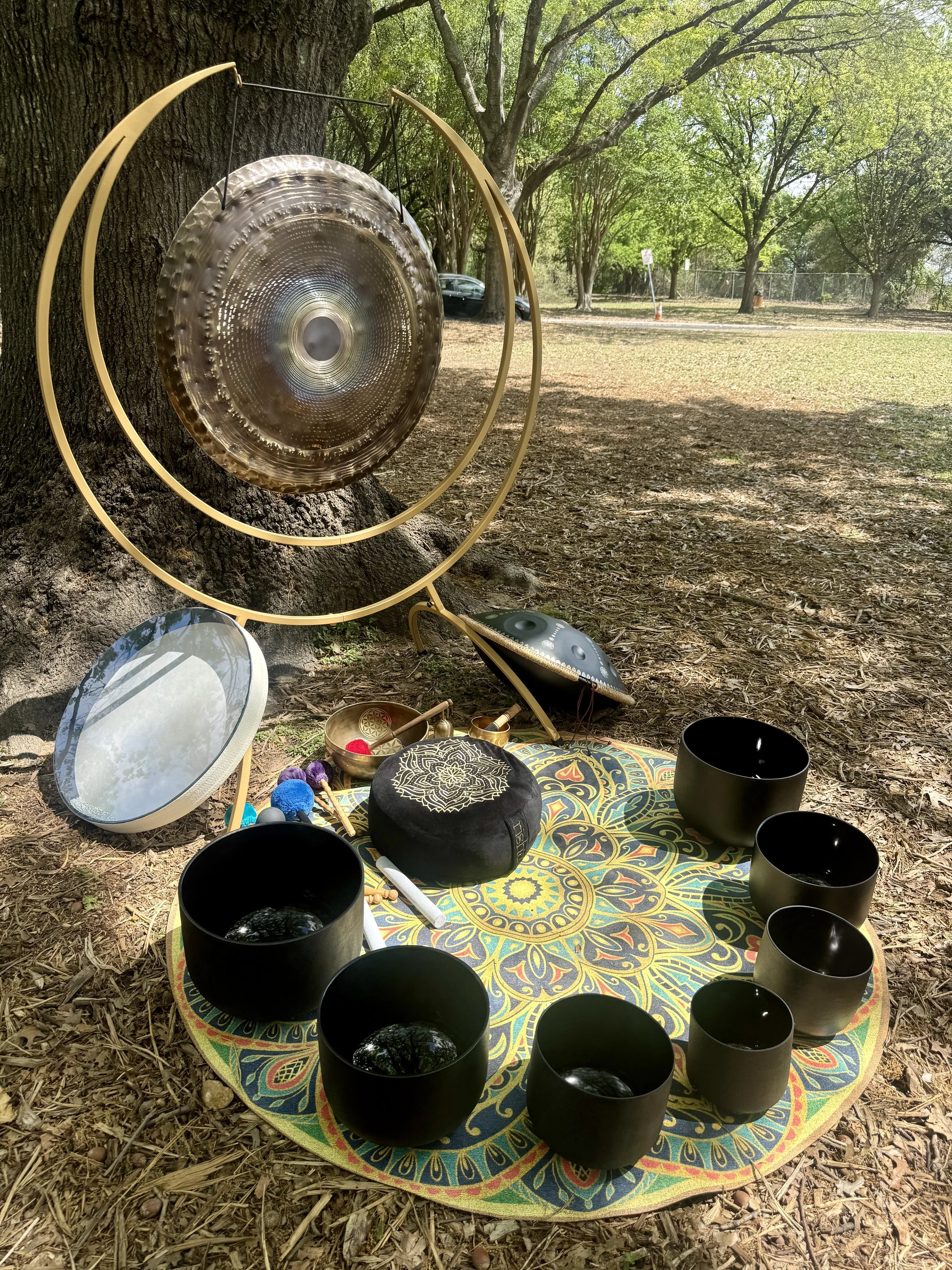 Crystal singing bowls, gong, chimes, and sound healing instruments arranged for an outdoor sound bath.