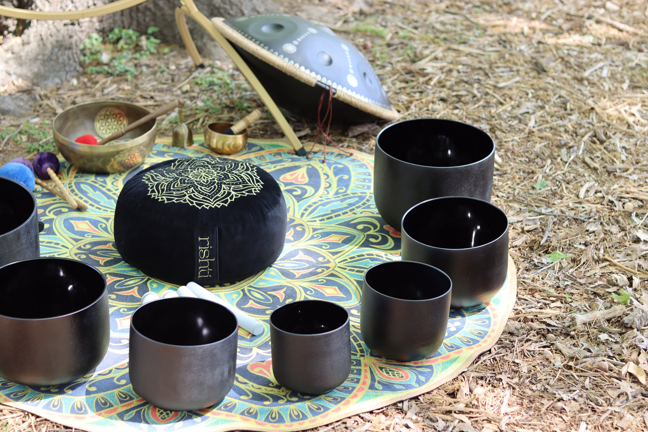 Meditation cushion, crystal singing bowls, and sound healing instruments arranged outdoors for mindful wellness practice