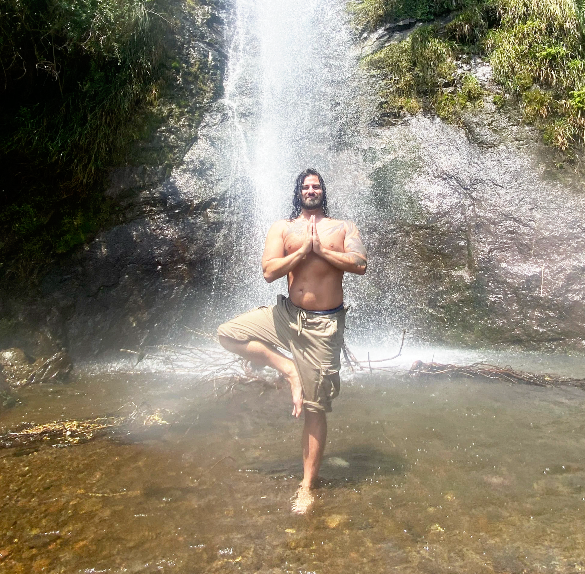 Jacob Madary practicing yoga meditation beneath a waterfall in a natural outdoor setting
